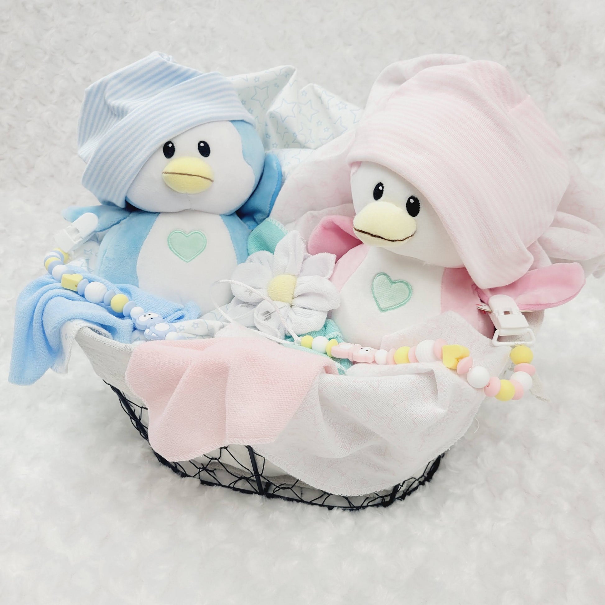 Ensemble cadeau pour babyshower de jumeaux garçon et fille. Un panier contenant des couvertures de flanelle 2 bonnets, des fleurs en débarbouillettes. complété de 2 attache-suce