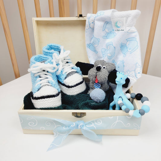 Ensemble cadeau dans un coffre de bois couleur naturelle. Contient une paire de pantoufle tricoté à la maison des débarbouillettes en forme de chien, un bavoir avec un coin en silicone et un jouet de dentition avec une girafe bleu