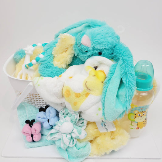 Ensemble cadeau pour babyshower. Un panier blanc contenant un toutou lapin turquoise, une super doudou avec un imprimé girafe, un biberon, des papillons et fleur fait en débarbouillettes. Complété par un jouet de dentition en silicone.