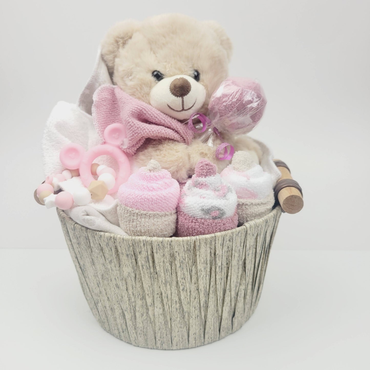 Ensemble cadeau pour babyshower de bébé fille. Un panier contenant un toutou ourson beige, une couverture en flanelle des débarbouillettes disposées en cupecake et des bas en forme de suçon. Complété d'un jouet de dentition en silicone.