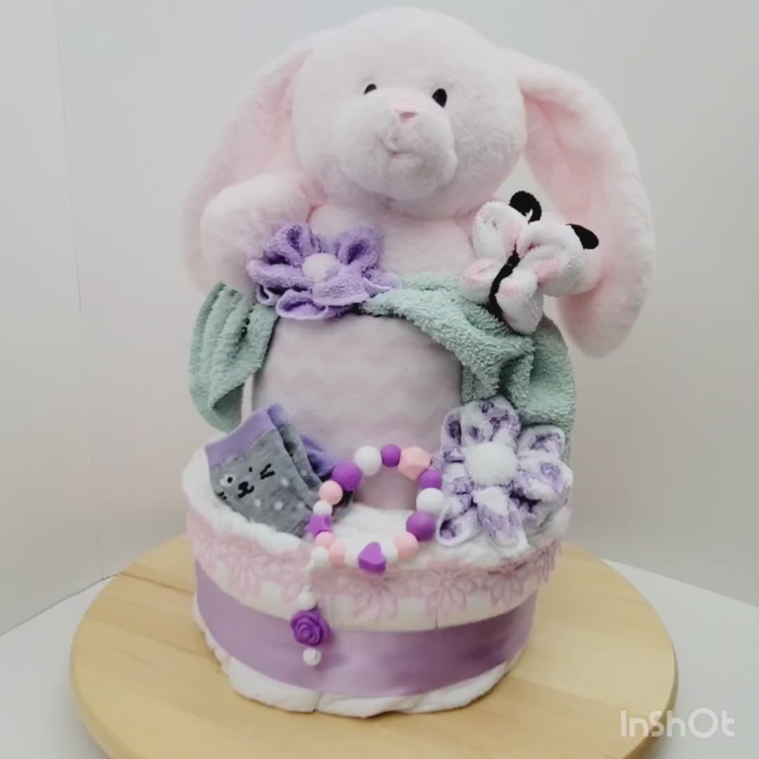 Vidéo 360 de l'Ensemble cadeau pour babyshower de bébé fille. Gâteau 2 étages avec un toutou lapin inséré dans l'étage du dessus. On retrouve des bas sur l'étage du bas ainsi qu'un jouet de dentition en silicone. Trouvez aussi les fleur fait en débarbouillettes et même le papillon.