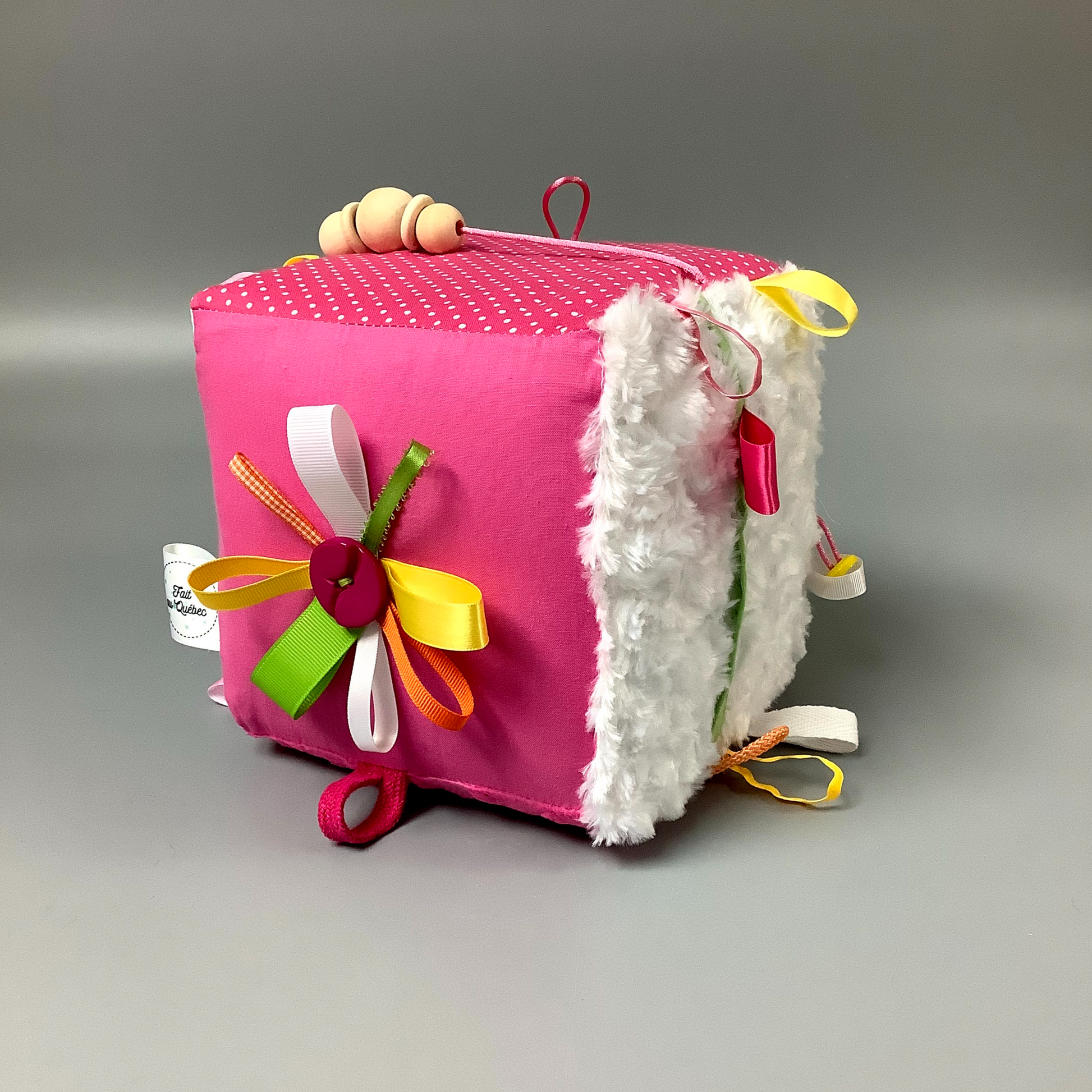 Cube d'éveil pour enfant  Fait en coton avec rubans et petits accessoires de bois. Le cube fait du bruit lorsqu'il est agité.  Ce produit unique est fait au Québec.