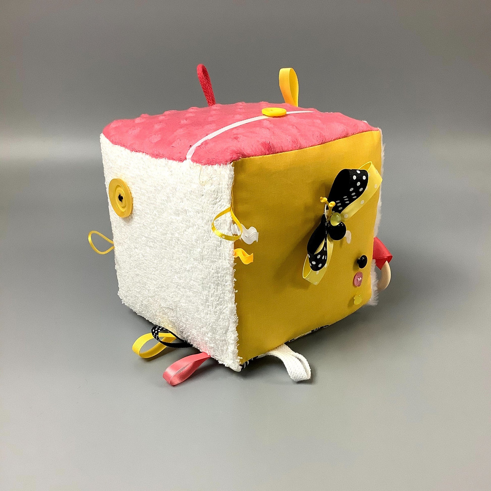 Cube d'éveil pour enfant  Fait en coton avec rubans et petits accessoires de bois. Le cube fait du bruit lorsqu'il est agité.  Ce produit unique est fait au Québec.