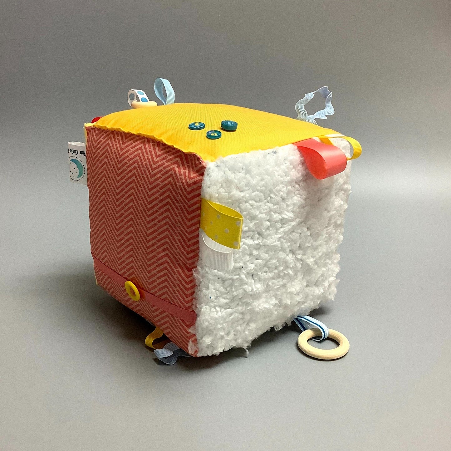 Cube d'éveil pour enfant Fait en coton avec rubans et petits accessoires de bois. Le cube fait du bruit lorsqu'il est agité. Ce produit unique est fait au Québec.