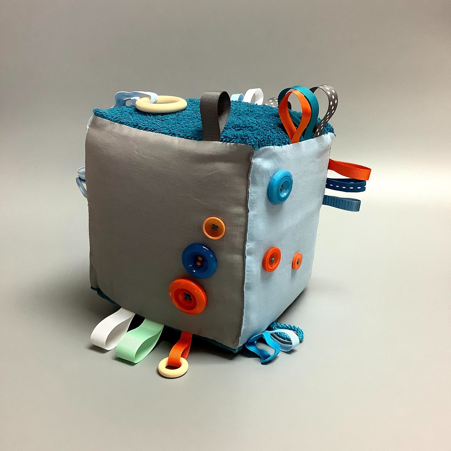 Cube d'éveil pour enfant Fait en coton avec rubans et petits accessoires de bois. Le cube fait du bruit lorsqu'il est agité. Ce produit unique est fait au Québec.