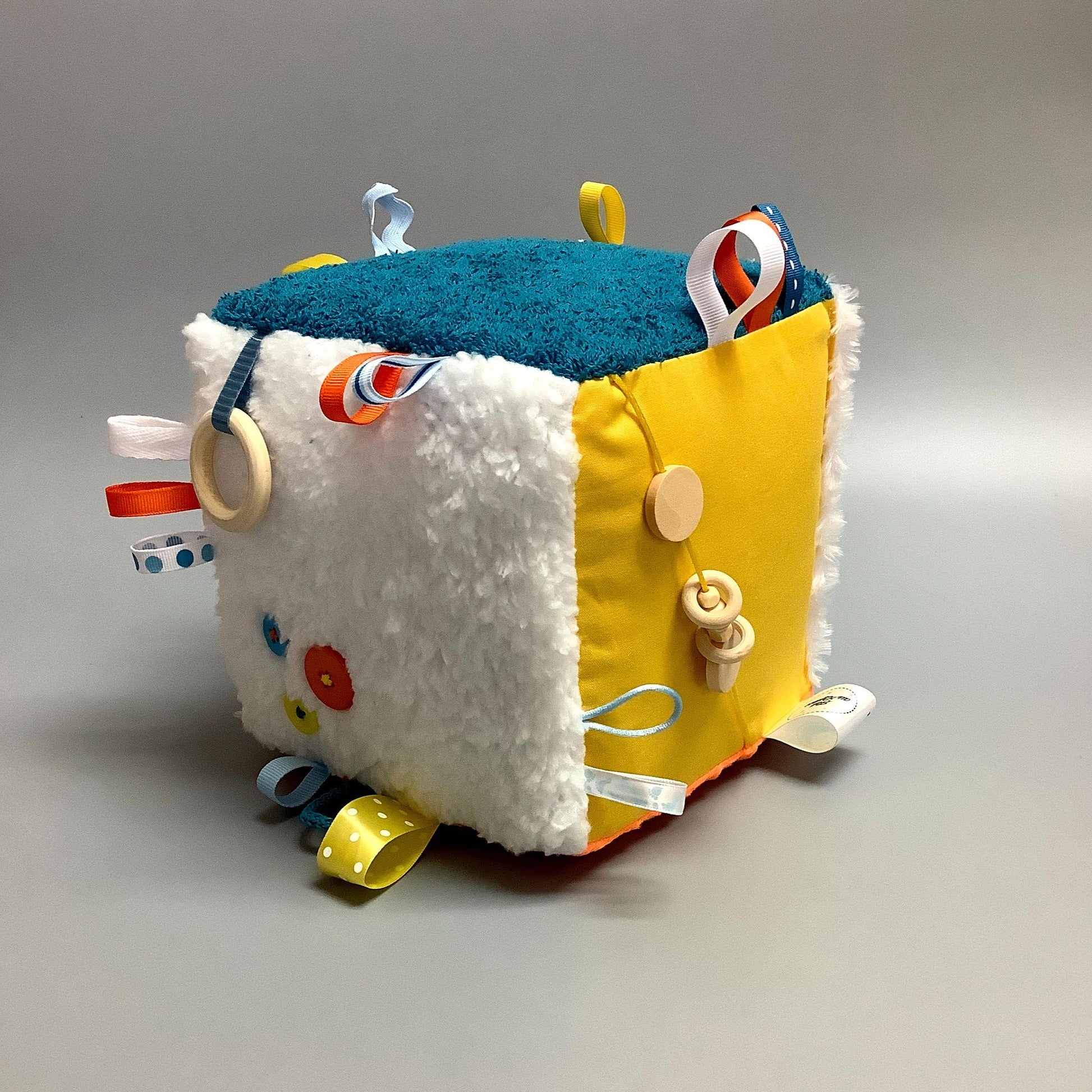Cube d'éveil pour enfant  Fait en coton avec rubans et petits accessoires de bois. Le cube fait du bruit lorsqu'il est agité.  Ce produit unique est fait au Québec.