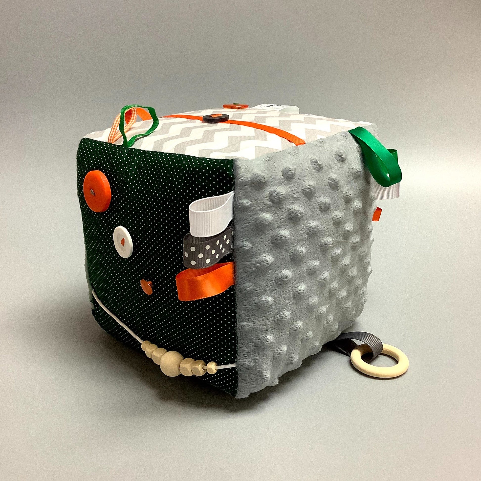 Cube d'éveil pour enfant  Fait en coton avec rubans et petits accessoires de bois. Le cube fait du bruit lorsqu'il est agité.  Ce produit unique est fait au Québec.