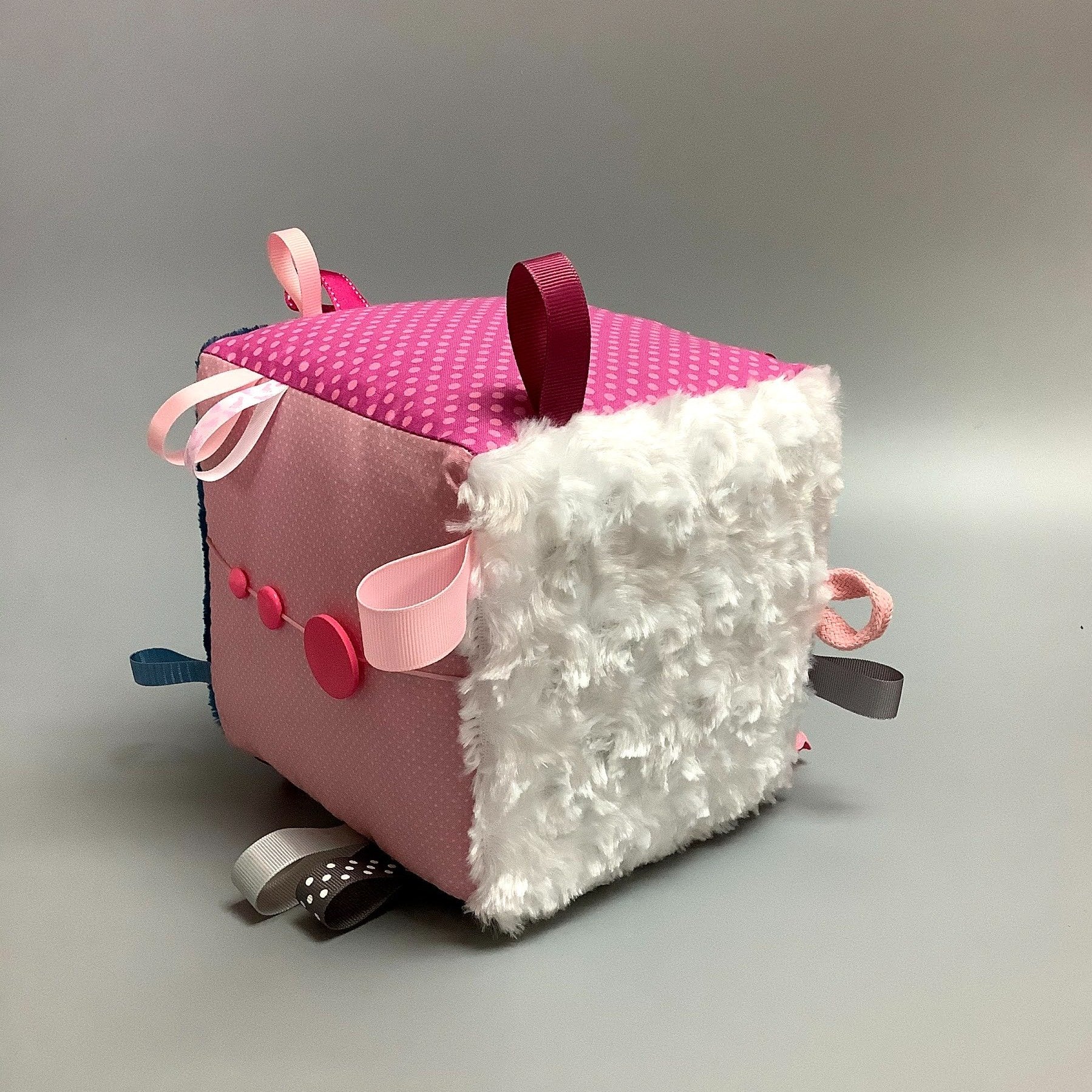 Cube d'éveil pour enfant  Fait en coton avec rubans et petits accessoires de bois. Le cube fait du bruit lorsqu'il est agité.  Ce produit unique est fait au Québec.
