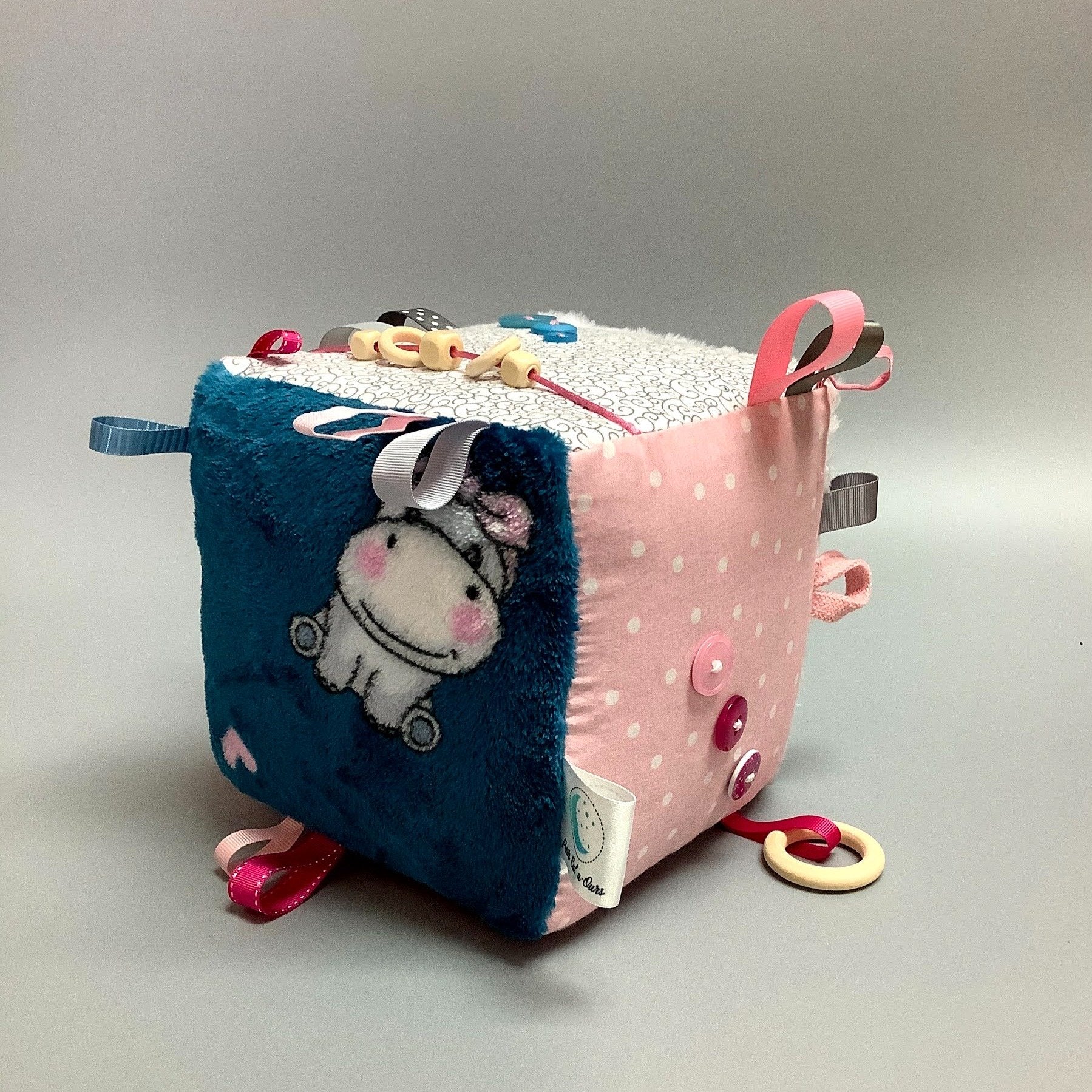 Cube d'éveil pour enfant  Fait en coton avec rubans et petits accessoires de bois. Le cube fait du bruit lorsqu'il est agité.  Ce produit unique est fait au Québec.