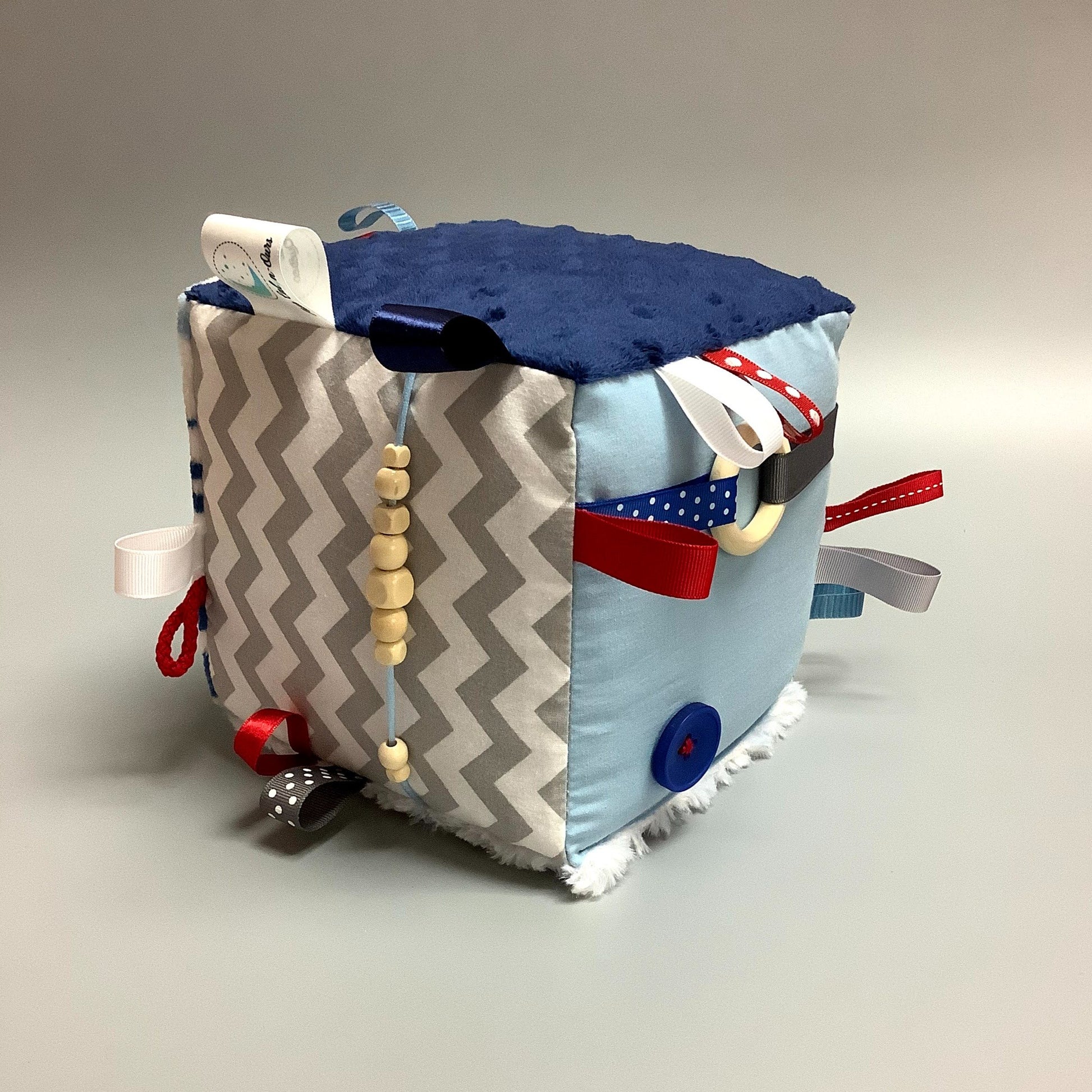 Cube d'éveil pour enfant  Fait en coton avec rubans et petits accessoires de bois. Le cube fait du bruit lorsqu'il est agité.  Ce produit unique est fait au Québec.