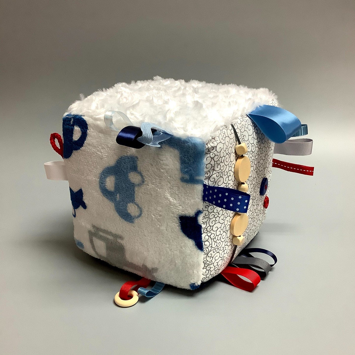 Cube d'éveil pour enfant  Fait en coton avec rubans et petits accessoires de bois. Le cube fait du bruit lorsqu'il est agité.  Ce produit unique est fait au Québec.
