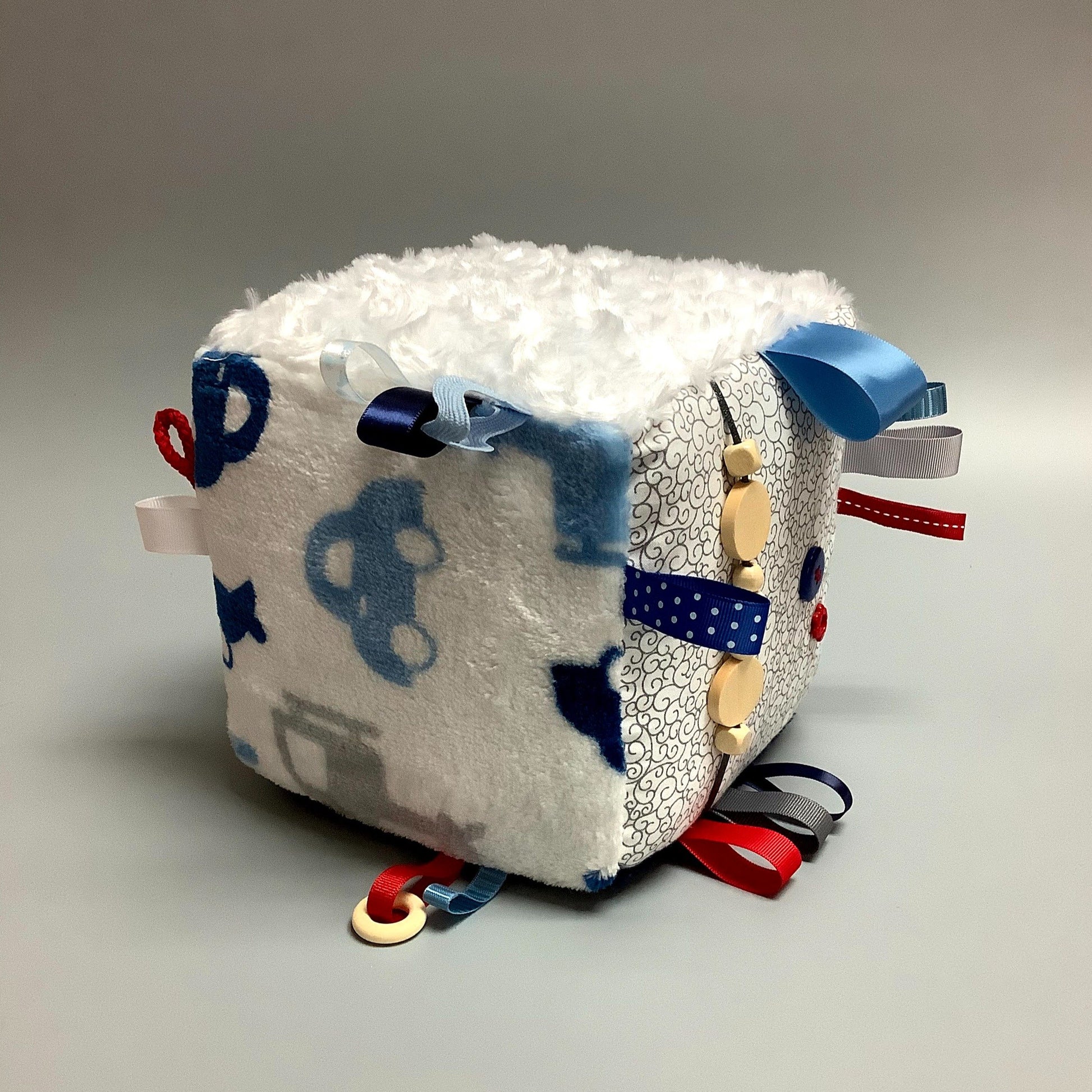 Cube d'éveil pour enfant  Fait en coton avec rubans et petits accessoires de bois. Le cube fait du bruit lorsqu'il est agité.  Ce produit unique est fait au Québec.