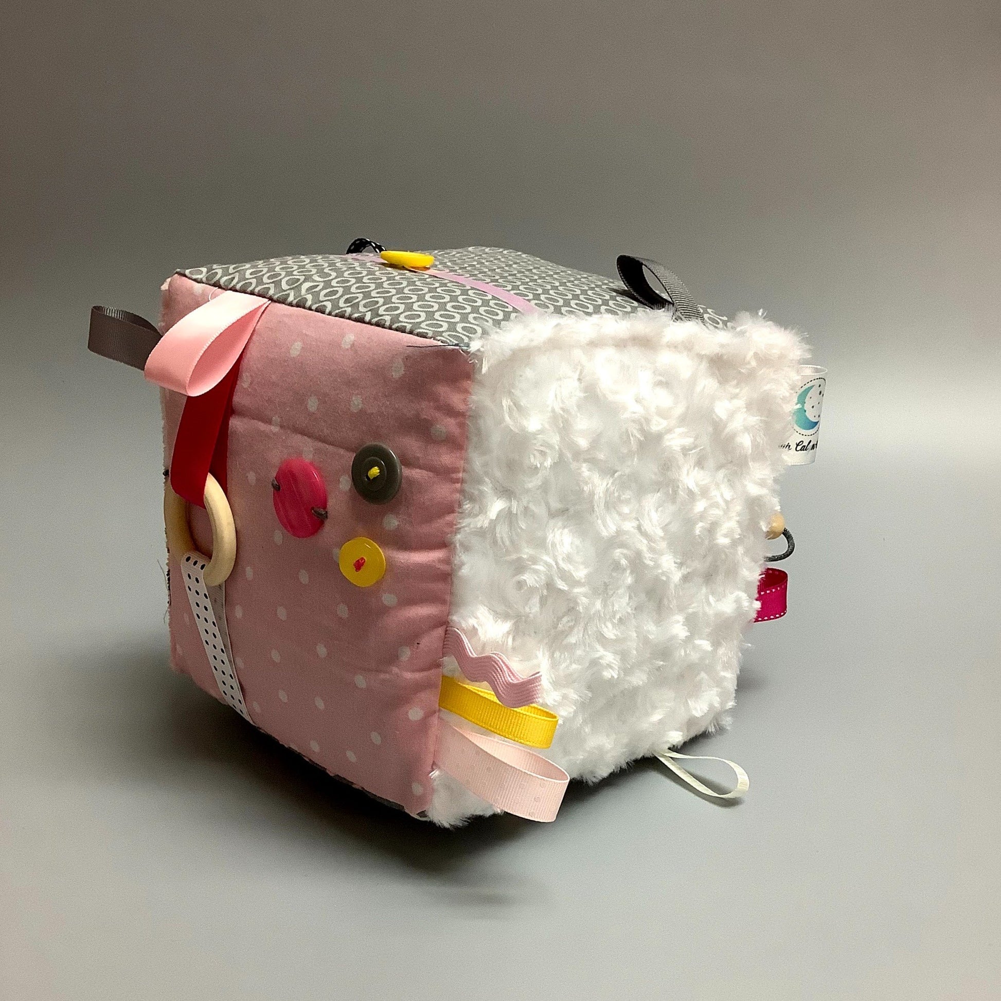 Cube d'éveil pour enfant  Fait en coton avec rubans et petits accessoires de bois. Le cube fait du bruit lorsqu'il est agité.  Ce produit unique est fait au Québec.