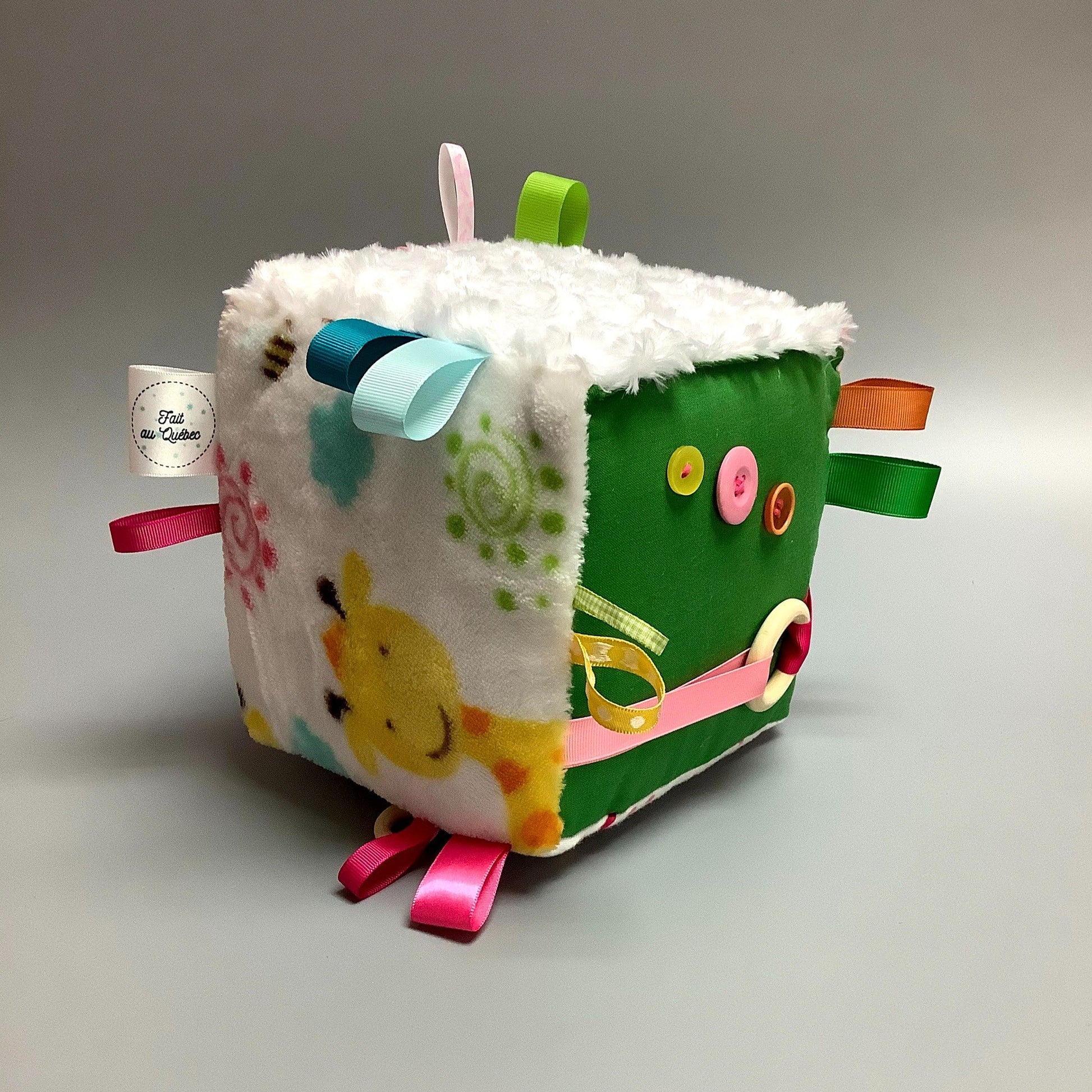 Cube d'éveil pour enfant  Fait en coton avec rubans et petits accessoires de bois. Le cube fait du bruit lorsqu'il est agité.  Ce produit unique est fait au Québec.
