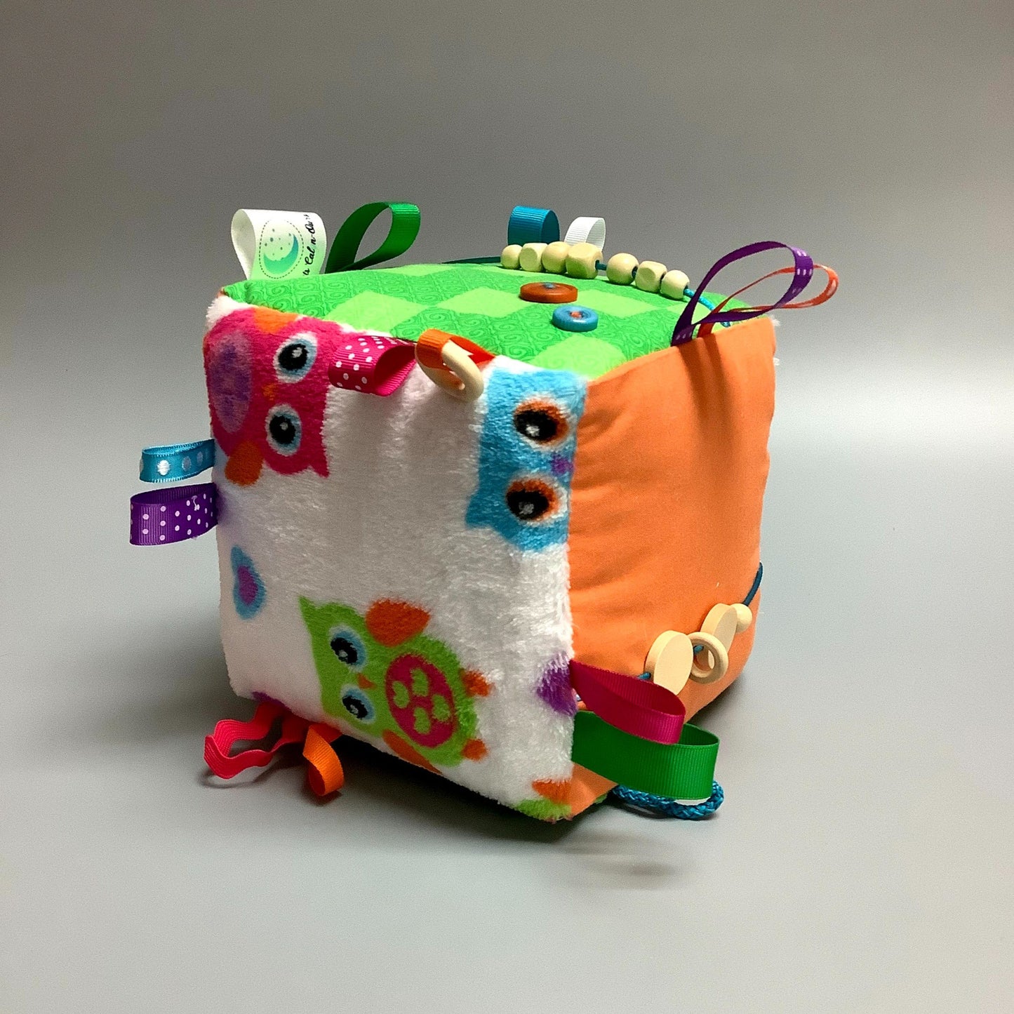 Cube d'éveil pour enfant  Fait en coton avec rubans et petits accessoires de bois. Le cube fait du bruit lorsqu'il est agité.  Ce produit unique est fait au Québec.