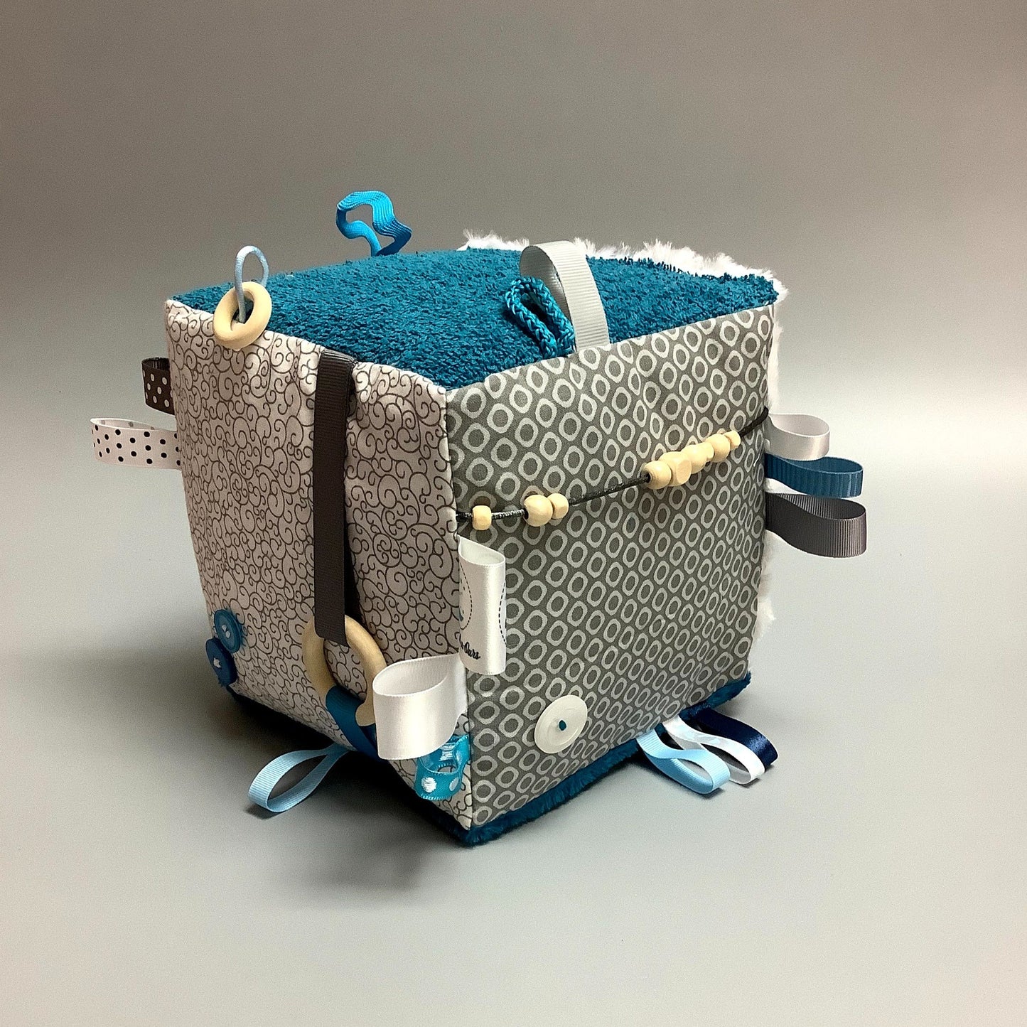 Cube d'éveil pour enfant Fait en coton avec rubans et petits accessoires de bois. Le cube fait du bruit lorsqu'il est agité. Ce produit unique est fait au Québec.