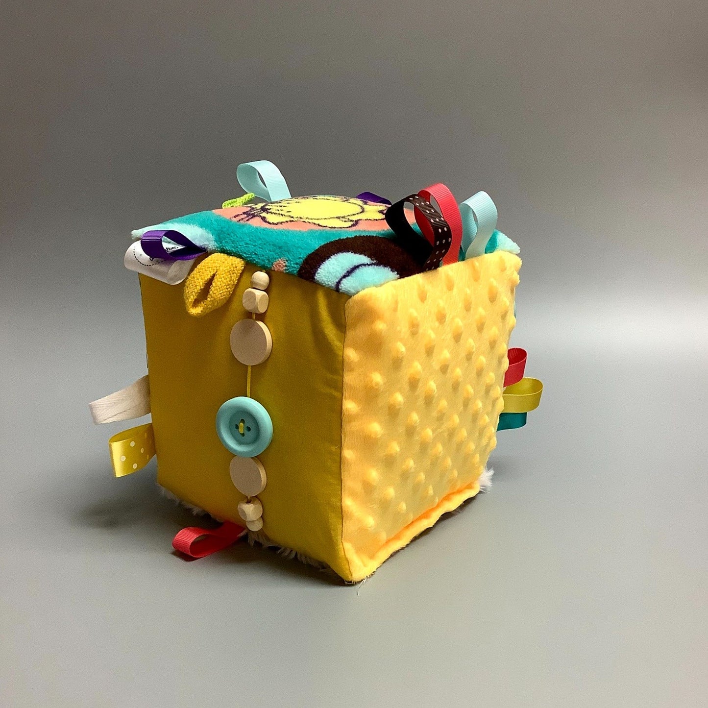 Cube d'éveil pour enfant  Fait en coton avec rubans et petits accessoires de bois. Le cube fait du bruit lorsqu'il est agité.  Ce produit unique est fait au Québec.