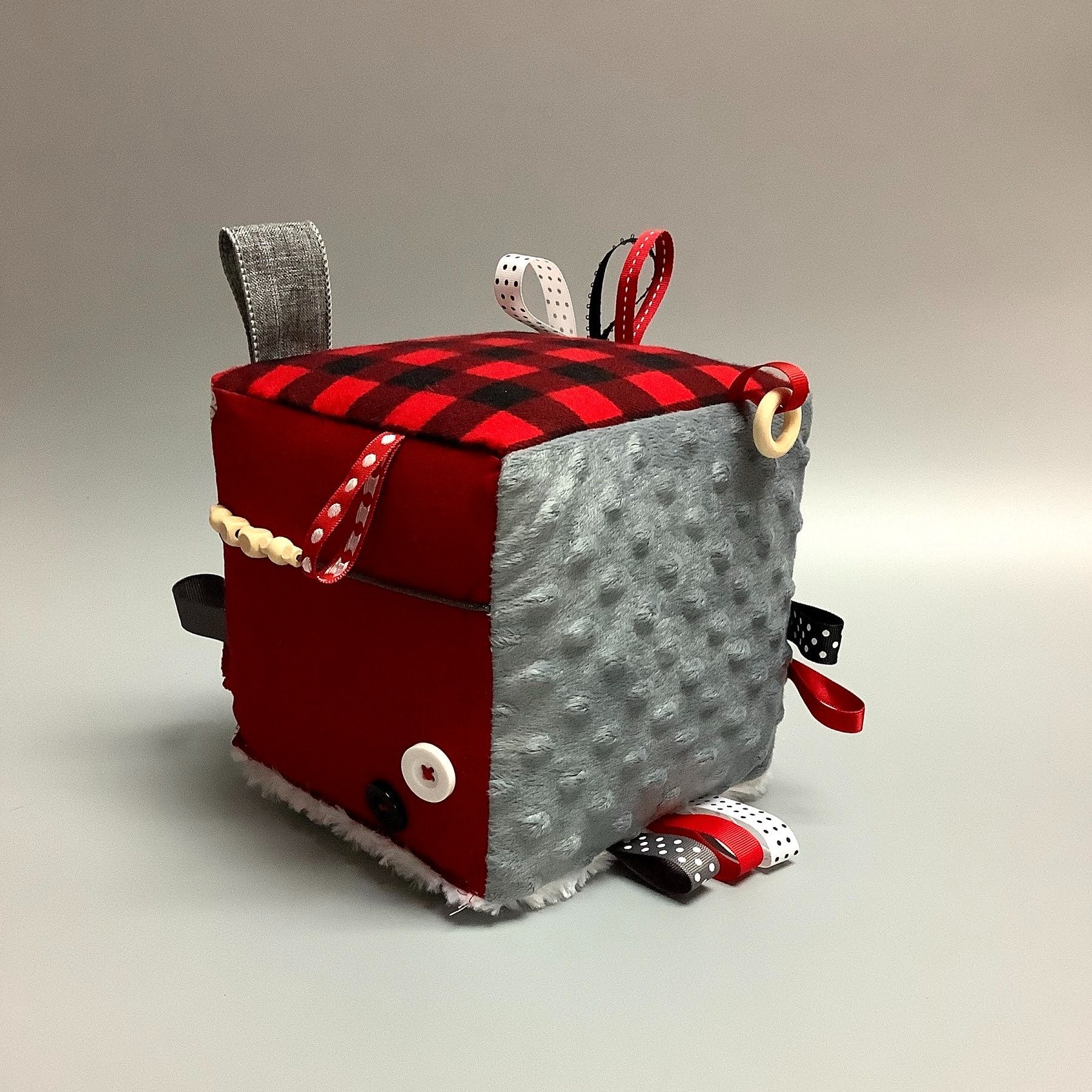 Cube d'éveil pour enfant  Fait en coton avec rubans et petits accessoires de bois. Le cube fait du bruit lorsqu'il est agité.  Ce produit unique est fait au Québec.