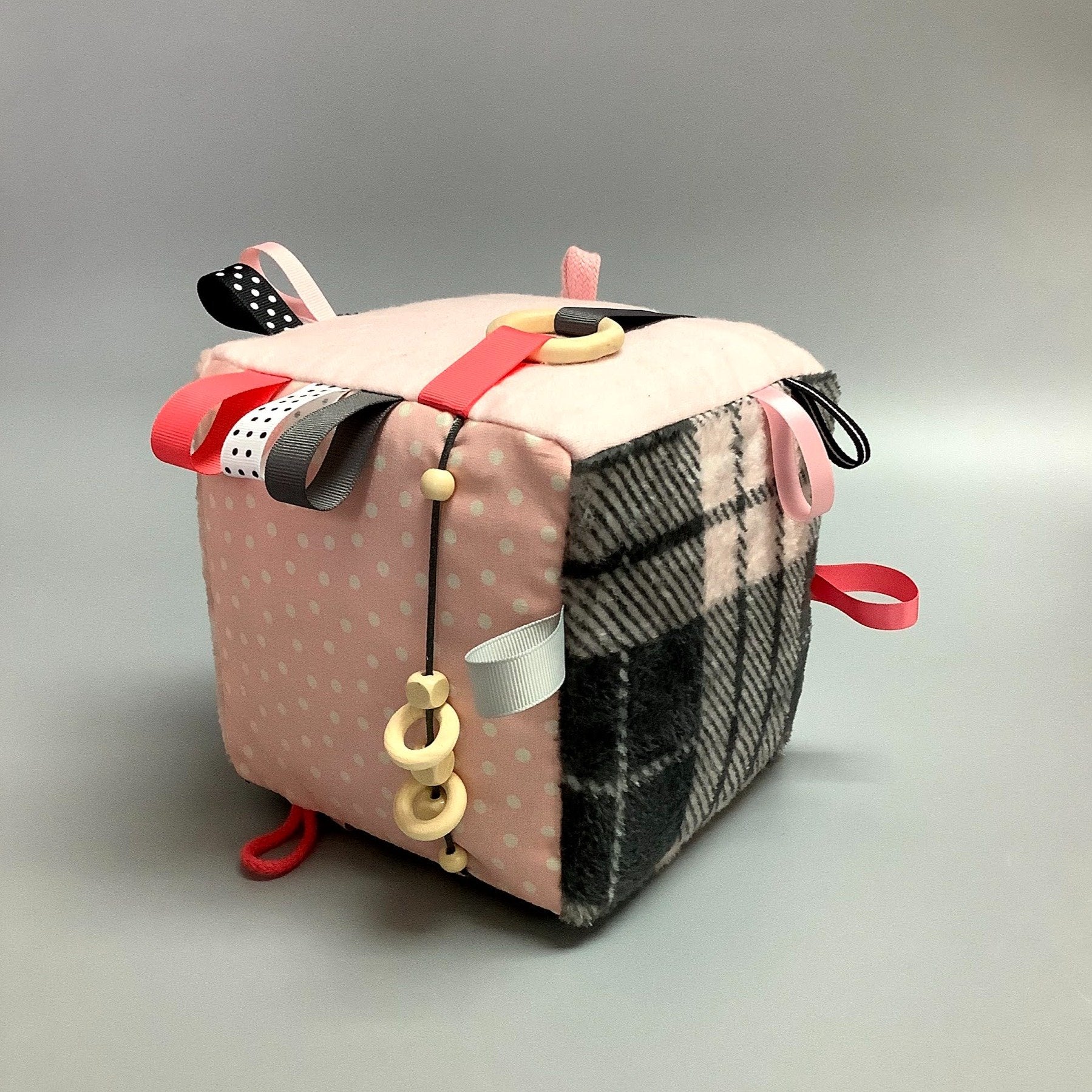 Cube d'éveil pour enfant  Fait en coton avec rubans et petits accessoires de bois. Le cube fait du bruit lorsqu'il est agité.  Ce produit unique est fait au Québec.