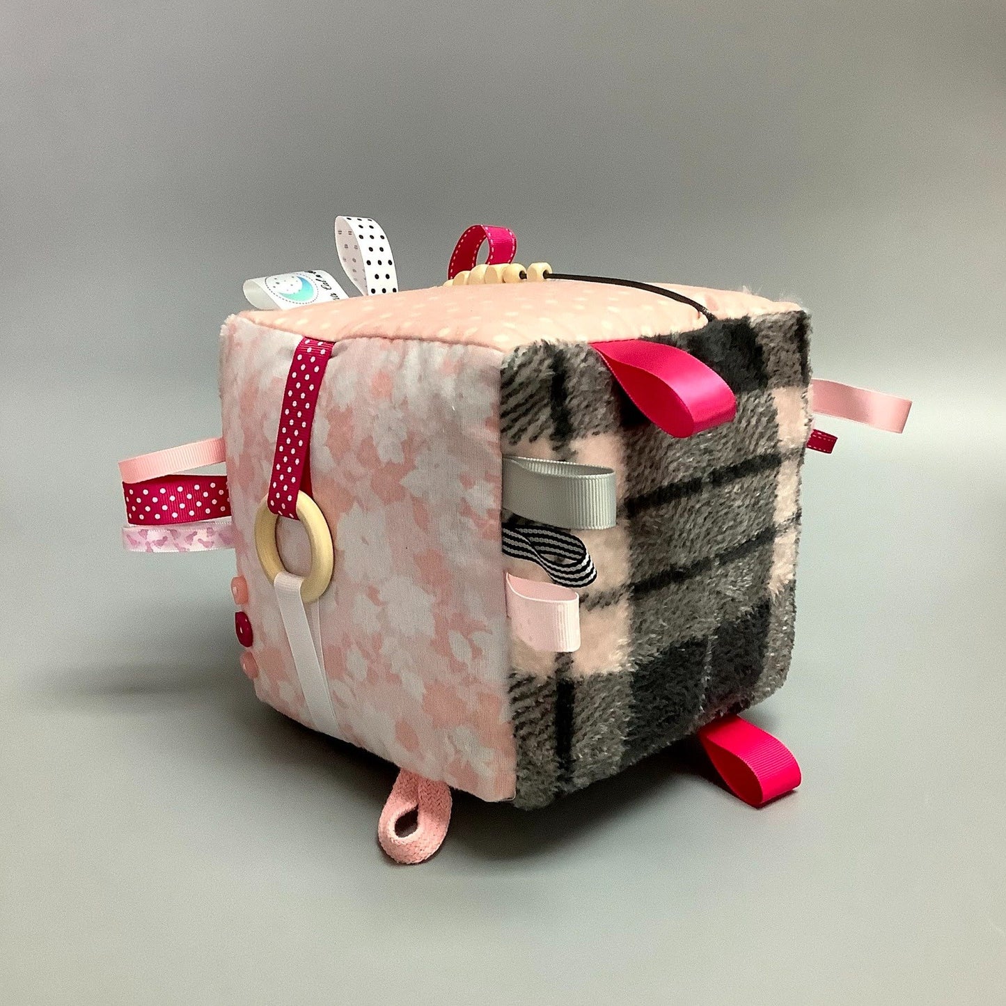 Cube d'éveil pour enfant  Fait en coton avec rubans et petits accessoires de bois. Le cube fait du bruit lorsqu'il est agité.  Ce produit unique est fait au Québec.