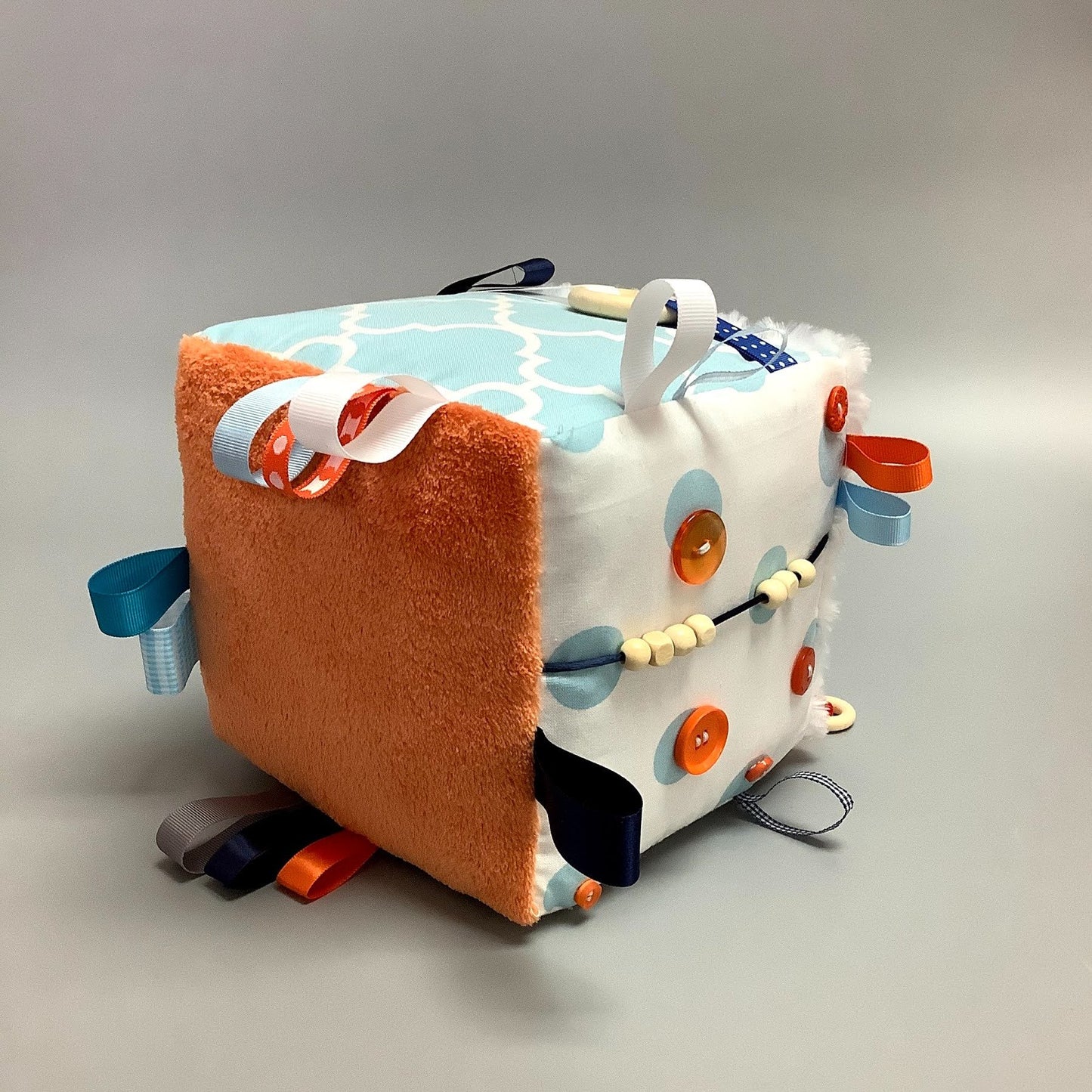 Cube d'éveil pour enfant  Fait en coton avec rubans et petits accessoires de bois. Le cube fait du bruit lorsqu'il est agité.  Ce produit unique est fait au Québec.
