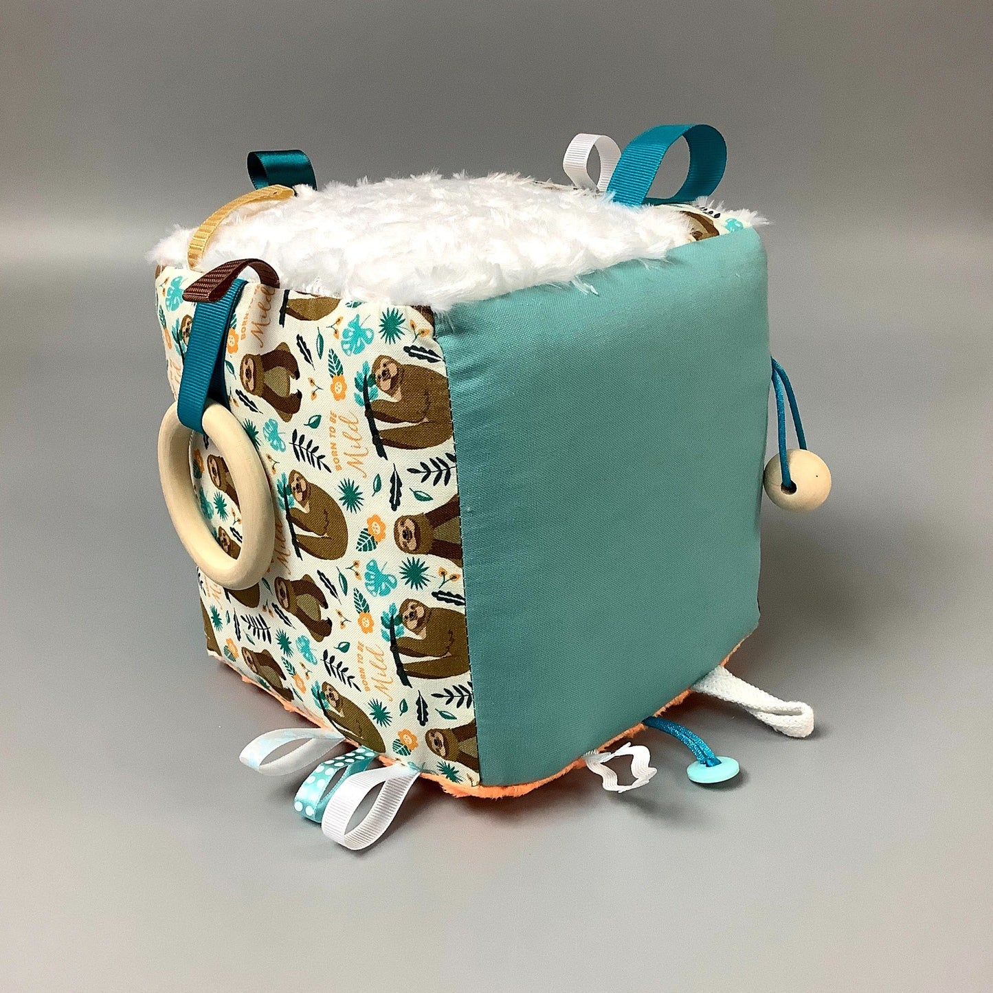 Cube d'éveil pour enfant  Fait en coton avec rubans et petits accessoires de bois. Le cube fait du bruit lorsqu'il est agité.  Ce produit unique est fait au Québec.