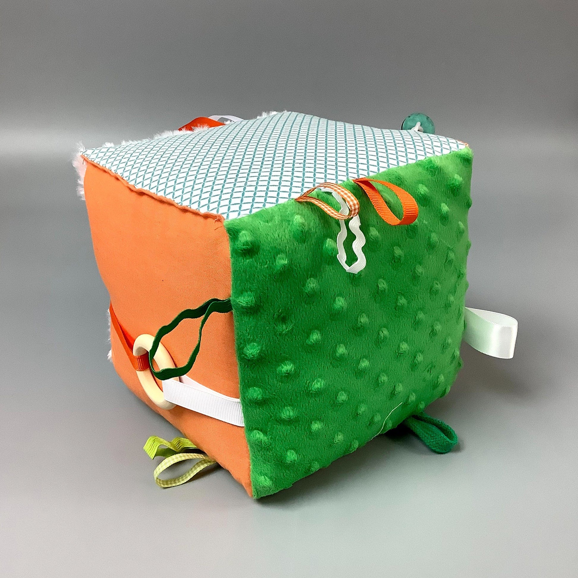 Cube d'éveil pour enfant  Fait en coton avec rubans et petits accessoires de bois. Le cube fait du bruit lorsqu'il est agité.  Ce produit unique est fait au Québec.