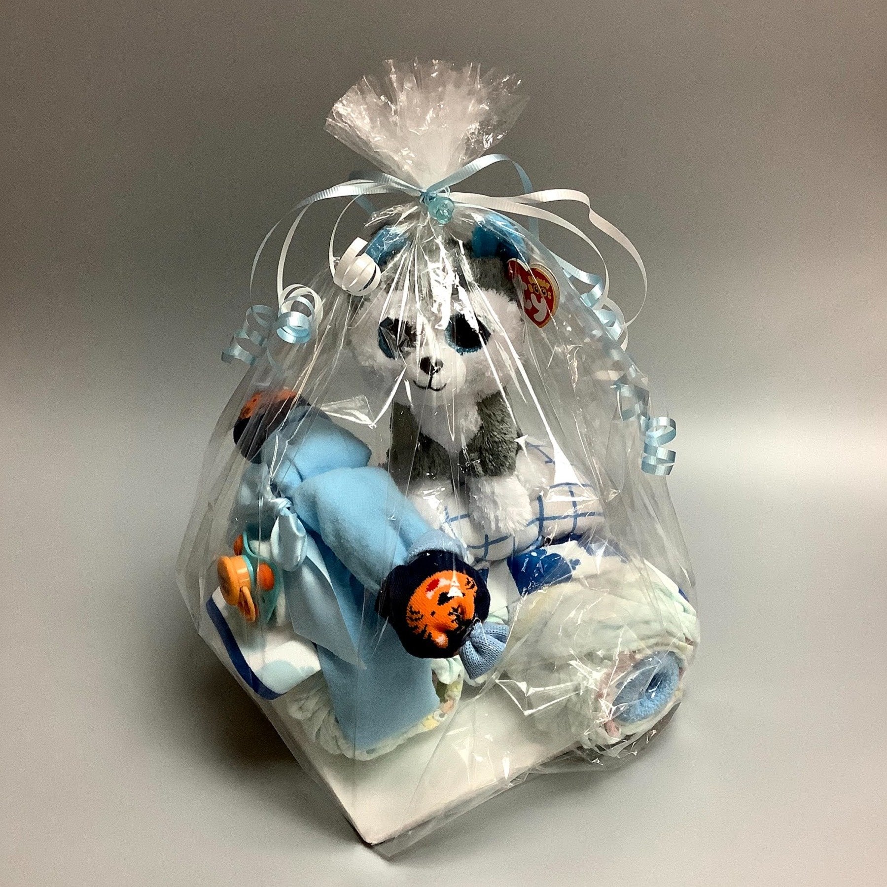 Ce gâteau contient :  - 20 couches (#2)  - 1 toutou de loup - 1 débarbouillettes 8'' x 8'' - 1 bavette  - 1 suce  - 2 paires de bas  - 1 doudou en flanelle 30'' x 30''  Ce produit est unique et fait ici au Québec