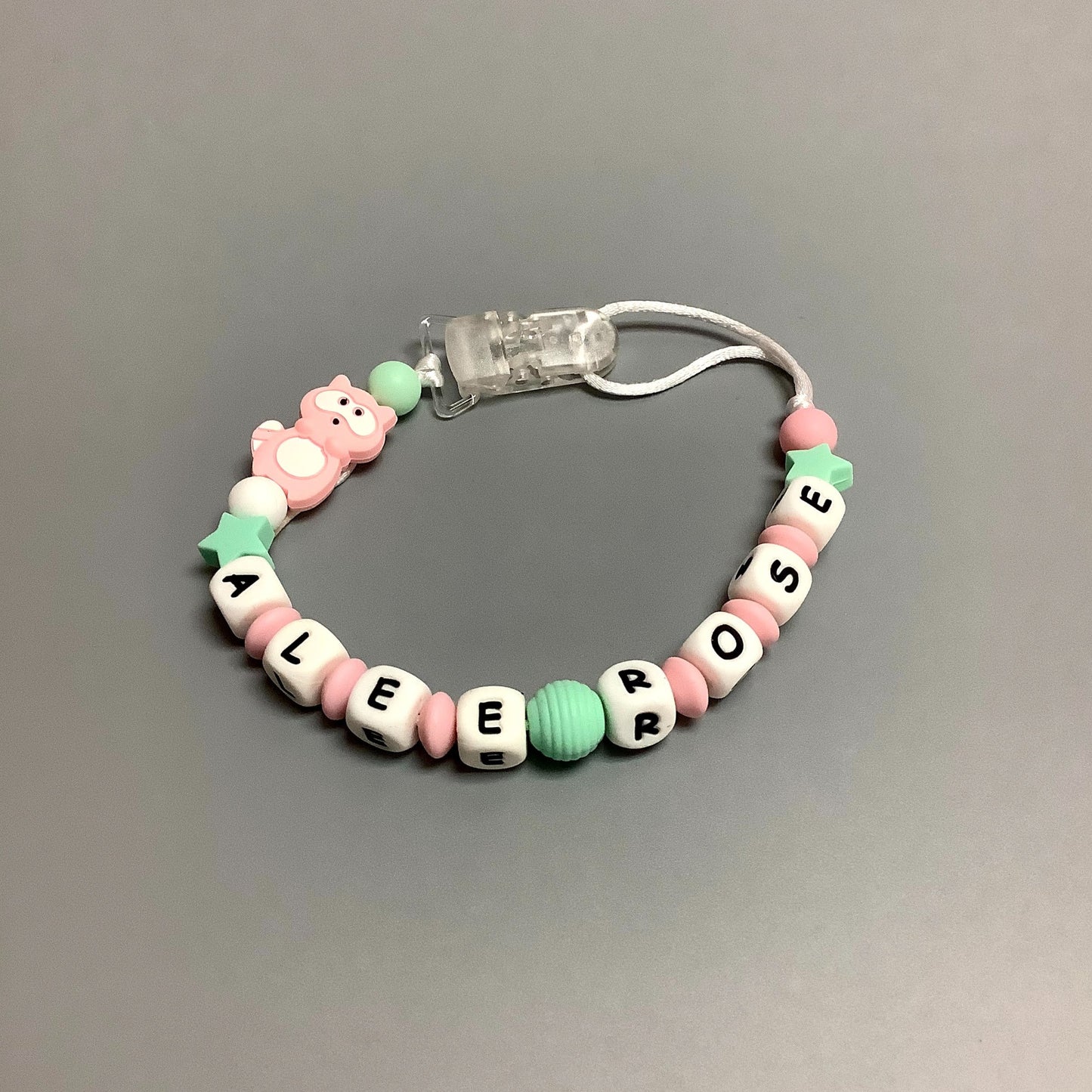 Jouet de dentition avec attache-suce fait avec plusieurs billes en silicones de différentes couleurs, tailles et formes, et il est complété par une attache en plastique