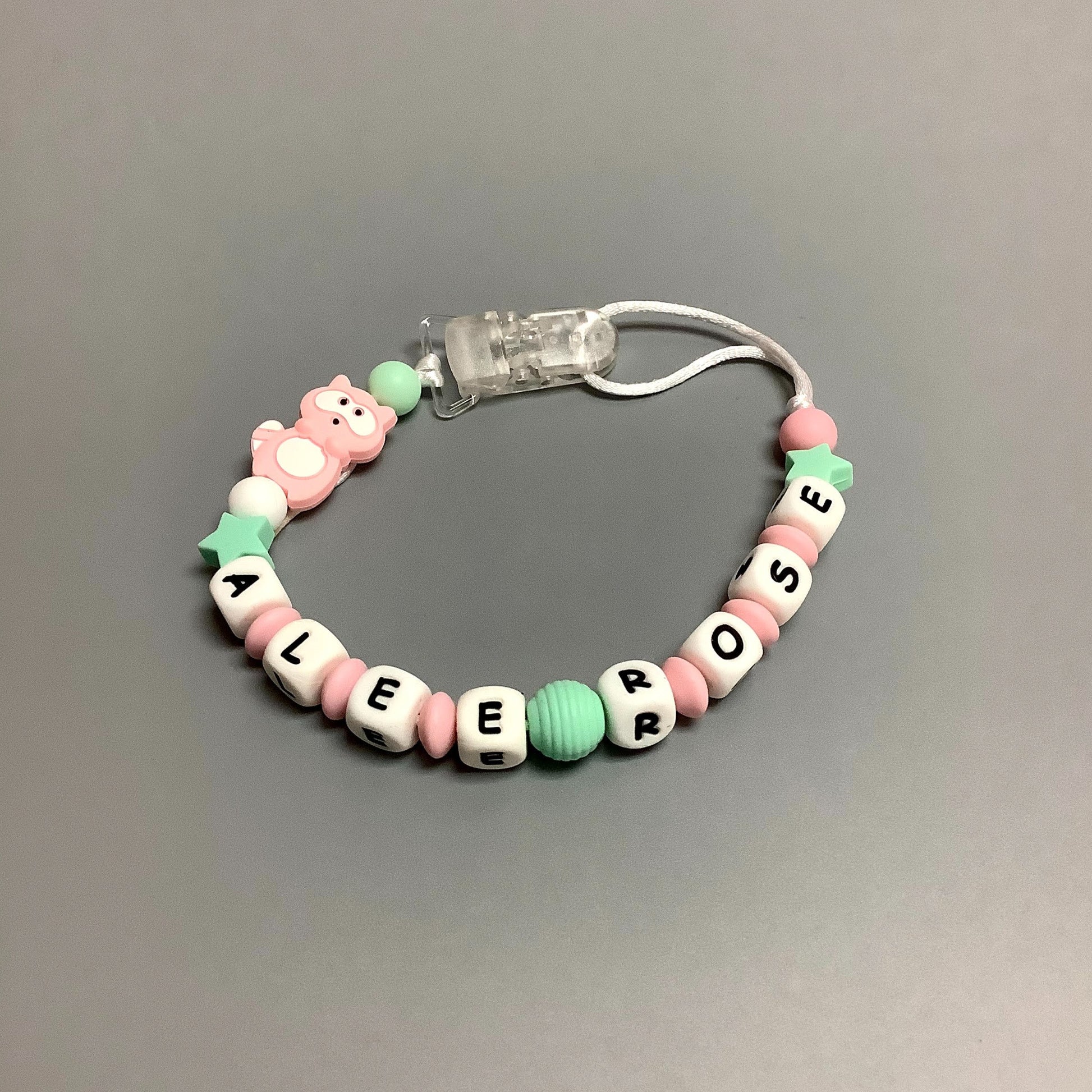 Jouet de dentition avec attache-suce fait avec plusieurs billes en silicones de différentes couleurs, tailles et formes, et il est complété par une attache en plastique