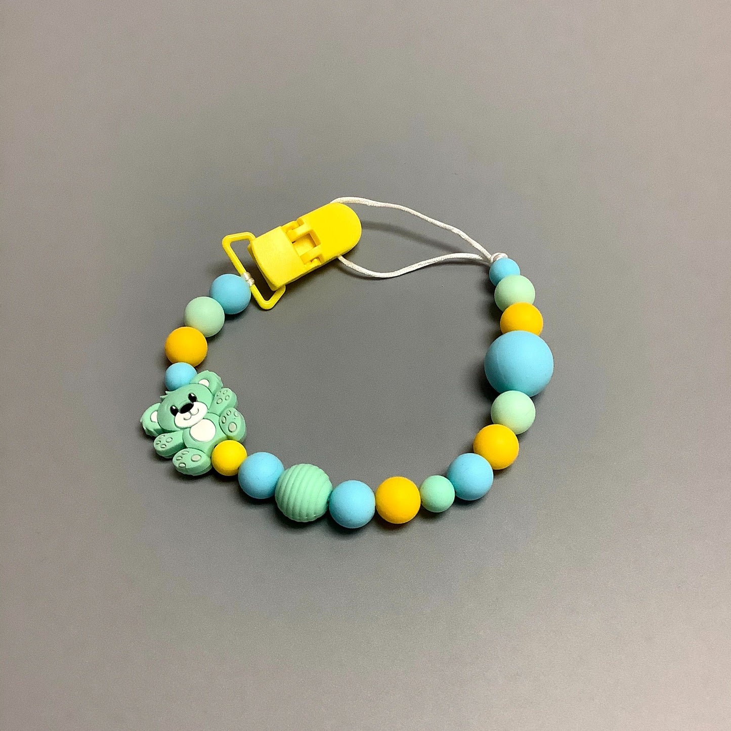 Jouet de dentition avec attache-suce fait avec plusieurs billes en silicones de différentes couleurs, tailles et formes, et il est complété par une attache en plastique