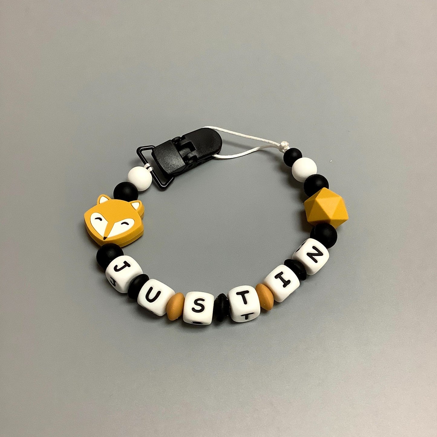 Jouet de dentition avec attache-suce fait avec plusieurs billes en silicones de différentes couleurs, tailles et formes, et il est complété par une attache en plastique