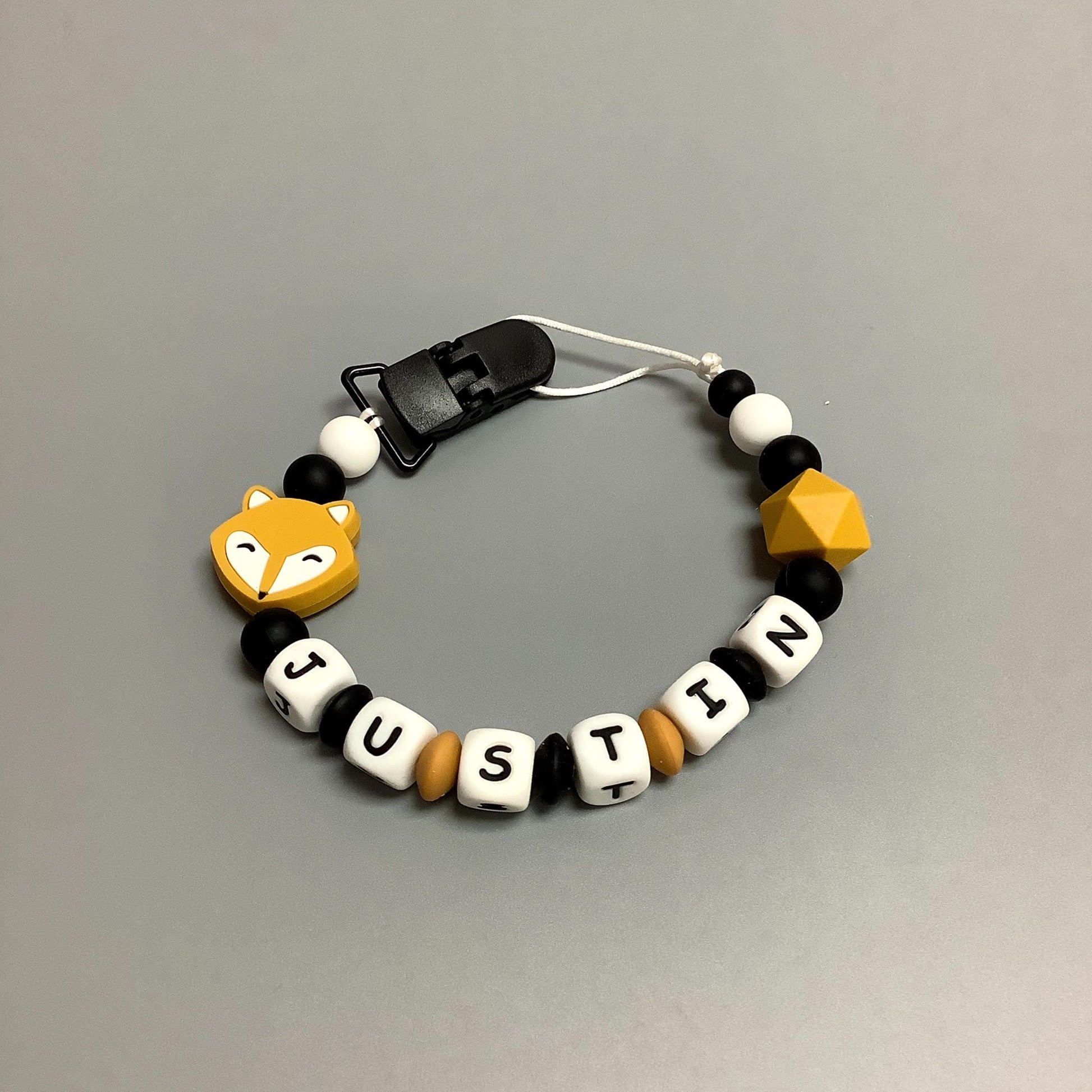 Jouet de dentition avec attache-suce fait avec plusieurs billes en silicones de différentes couleurs, tailles et formes, et il est complété par une attache en plastique