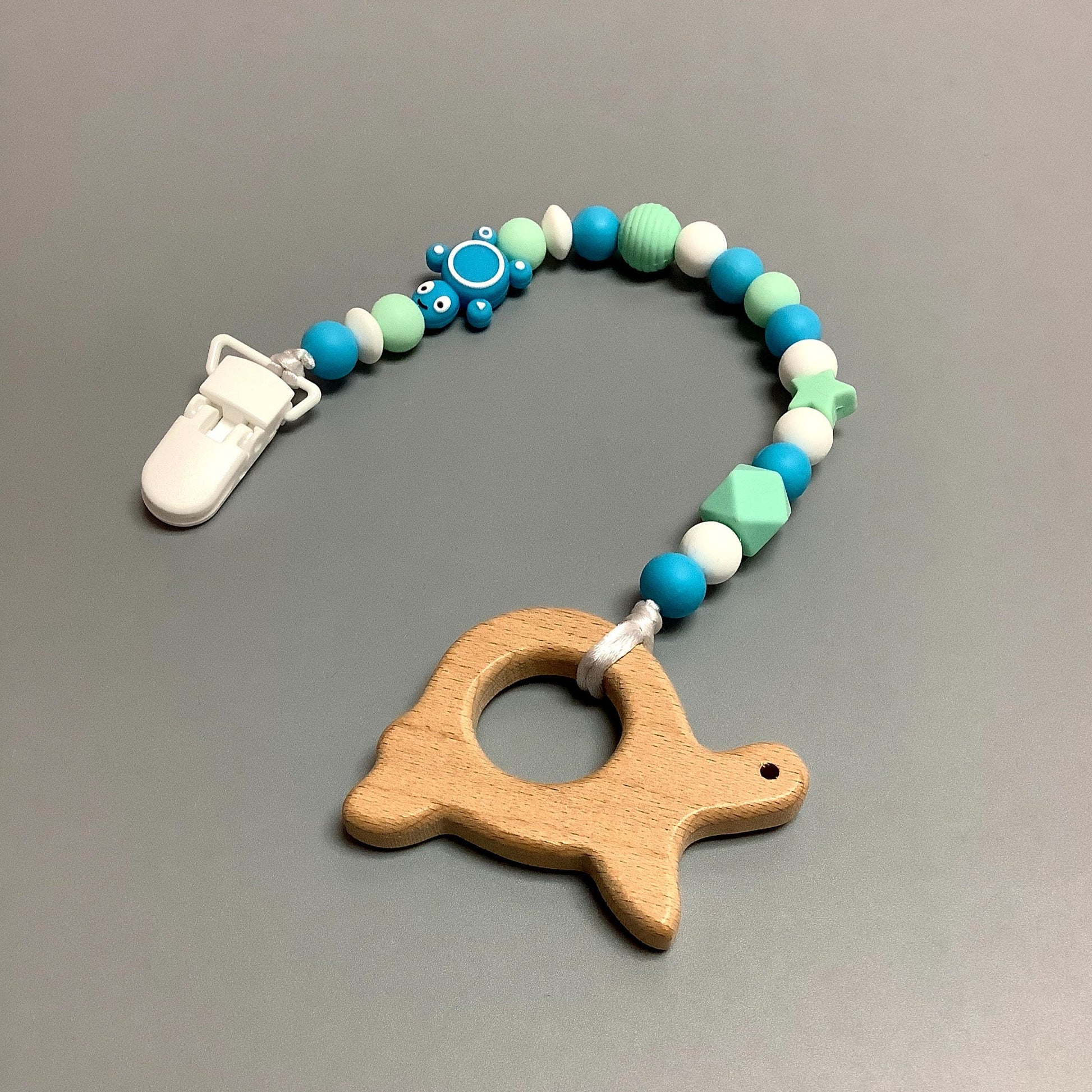 Jouet de dentition avec attache-suce fait avec plusieurs billes en silicones de différentes couleurs, tailles et formes, et il est complété par une attache en plastique