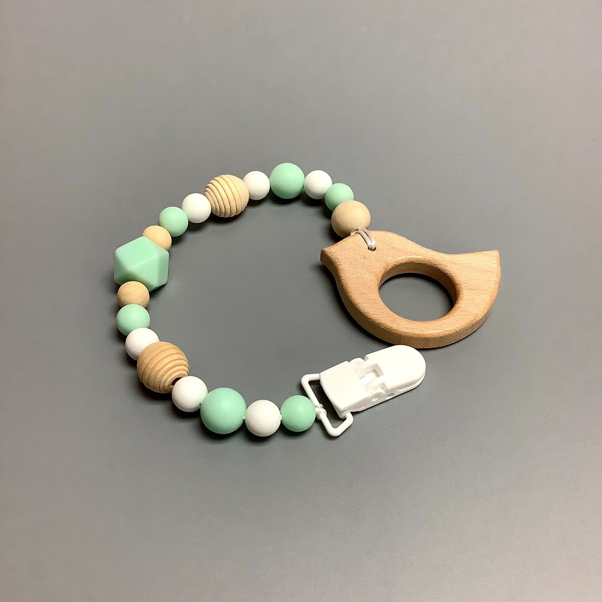 Jouet de dentition avec attache-suce fait avec plusieurs billes en silicones de différentes couleurs, tailles et formes, et il est complété par une attache en plastique.