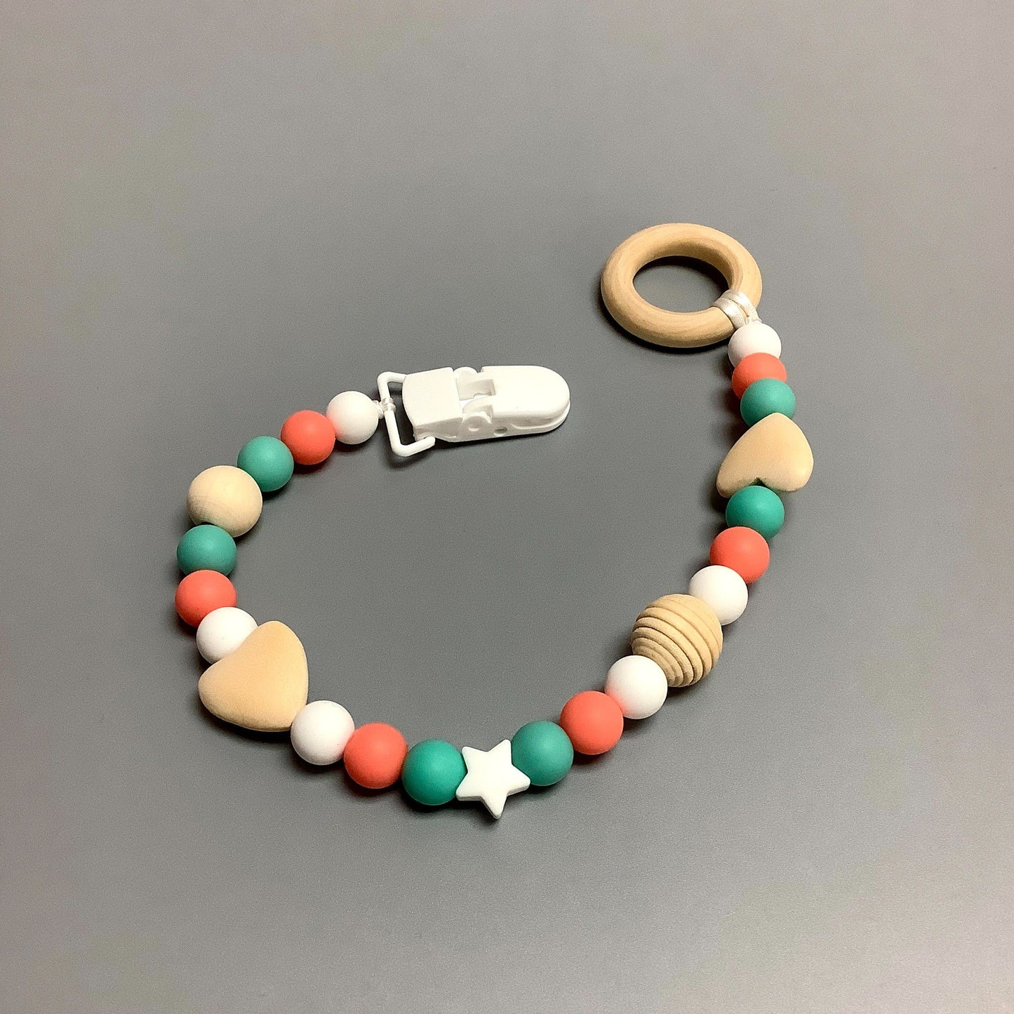 Jouet de dentition avec attache-suce fait avec plusieurs billes en silicones de différentes couleurs, tailles et formes, et il est complété par une attache en plastique.