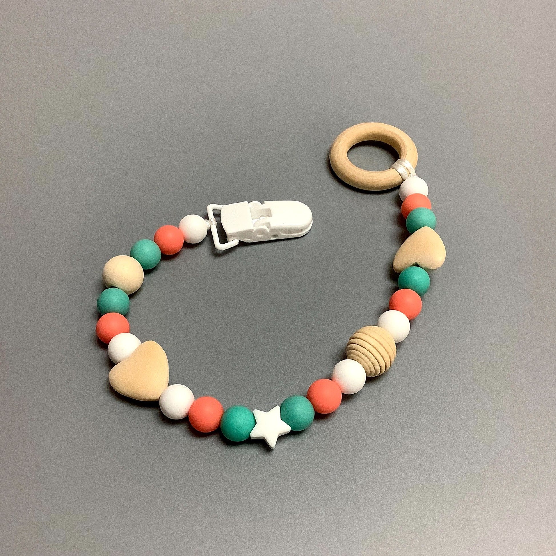 Jouet de dentition avec attache-suce fait avec plusieurs billes en silicones de différentes couleurs, tailles et formes, et il est complété par une attache en plastique.