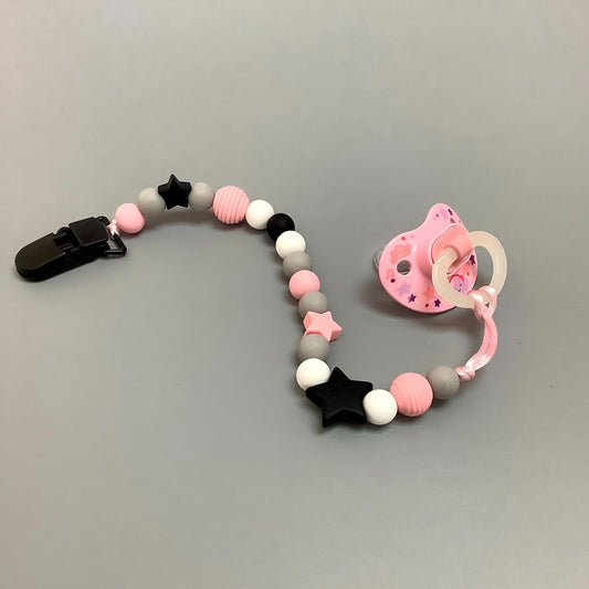 Attache-suce en silicone fait avec plusieurs billes en silicones de différentes couleurs, tailles et formes, et il est complété par une attache en plastique.