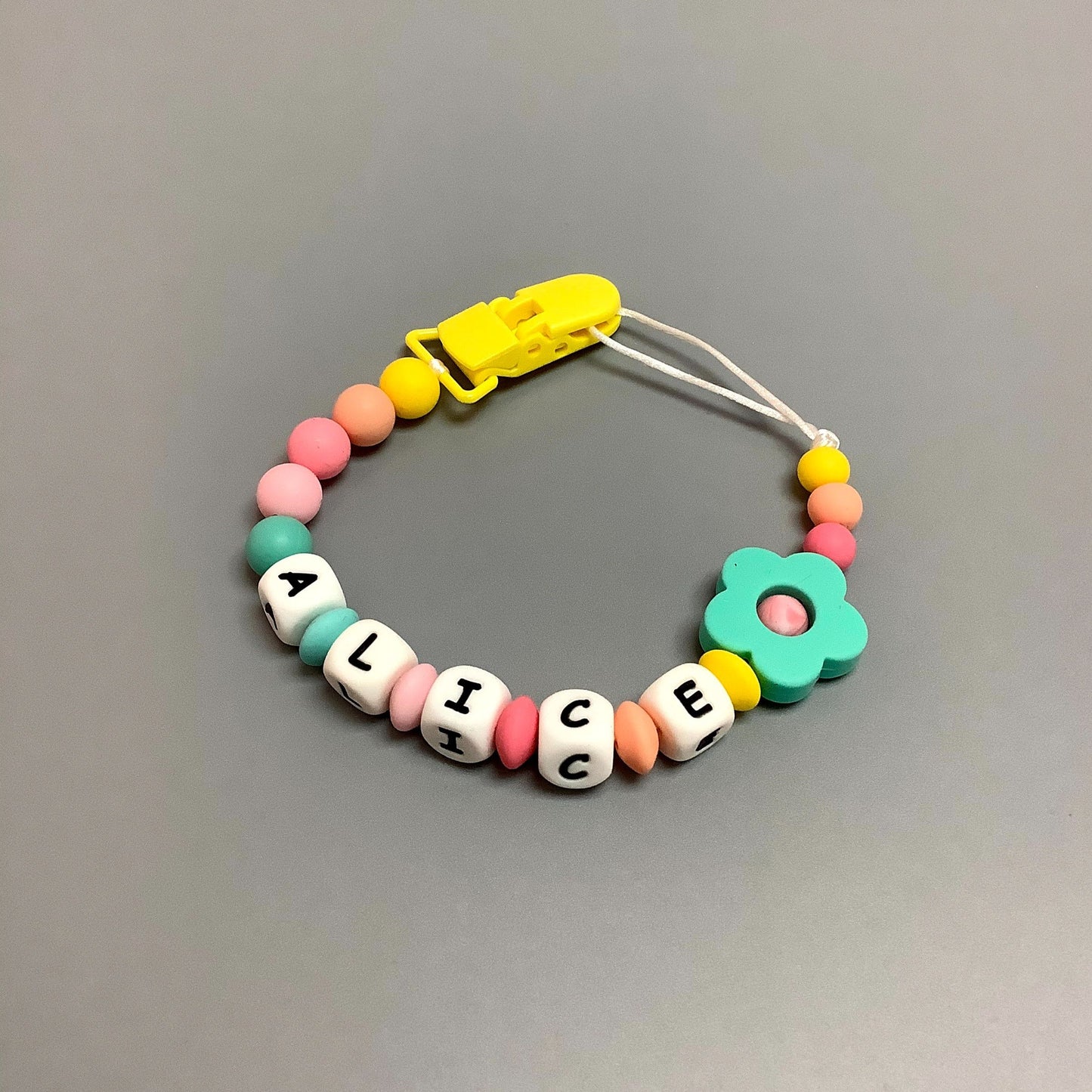 Jouet de dentition avec attache-suce fait avec plusieurs billes en silicones de différentes couleurs, tailles et formes, et il est complété par une attache en plastique