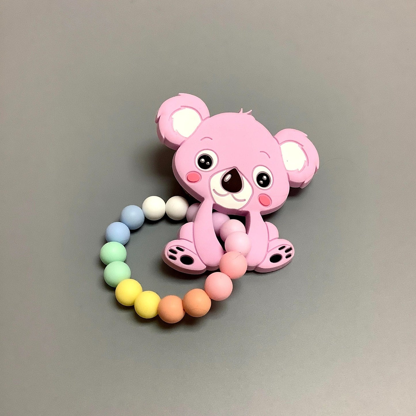 Attache-suce en silicone fait avec plusieurs billes en silicones de différentes couleurs, tailles et formes, et il est complété par une attache en plastique.