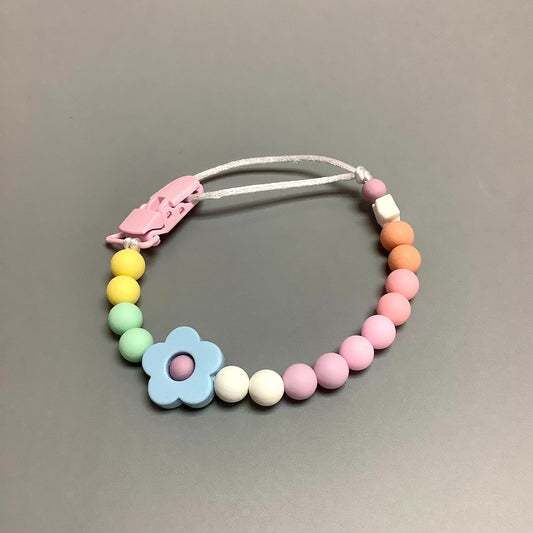 Attache-suce en silicone fait avec plusieurs billes en silicones de différentes couleurs, tailles et formes, et il est complété par une attache en plastique.