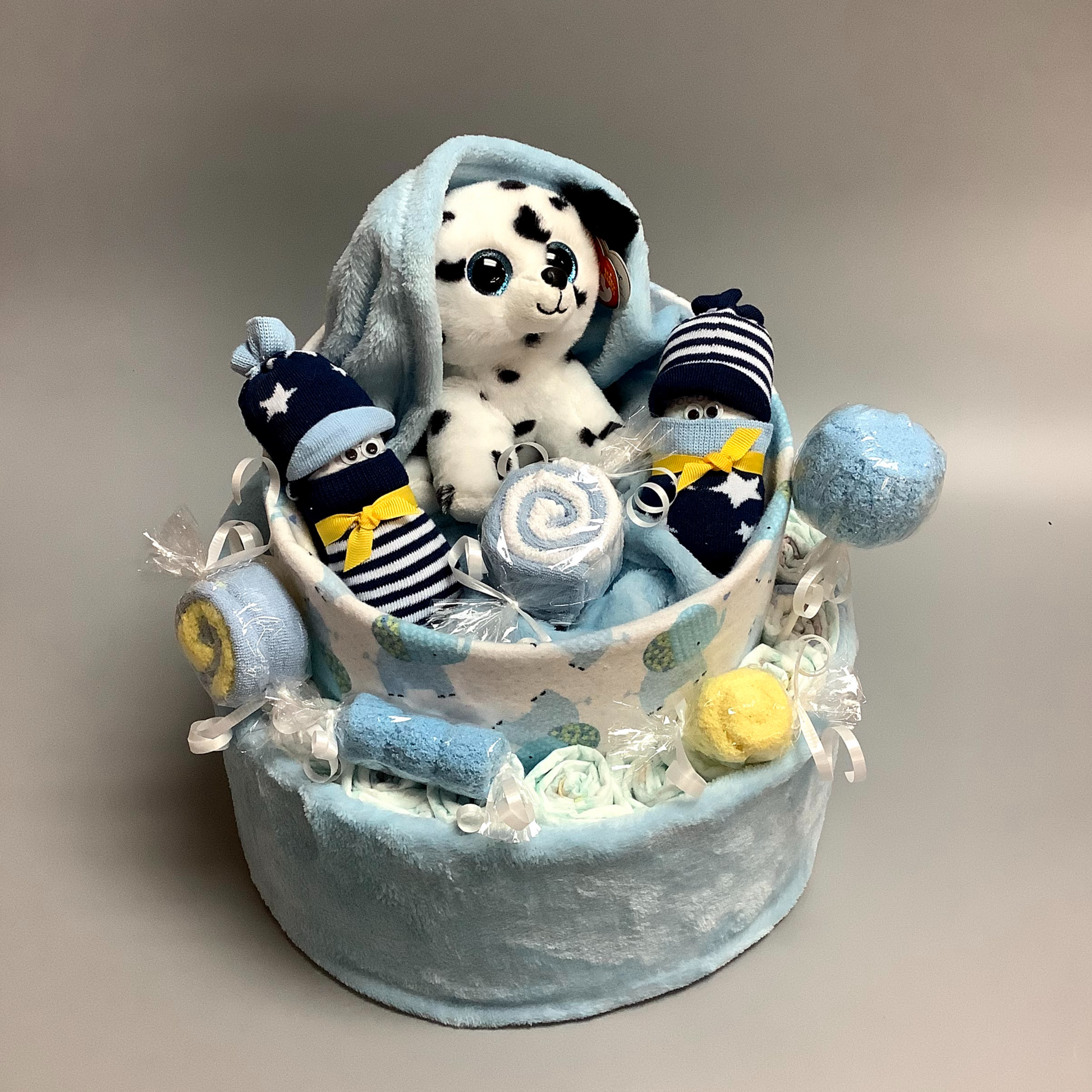 Ce gâteau contient :  - 15 couches (#2)  - 4 paires de bas  - 3 débarbouillettes (8''x8'')  - 1 doudou en flannelette avec des éléphants (30''x30'')  - 1 doudou en polars bleu (50''x34'')  - 1 toutou de chien   Ce produit est unique et fait ici au Québec,