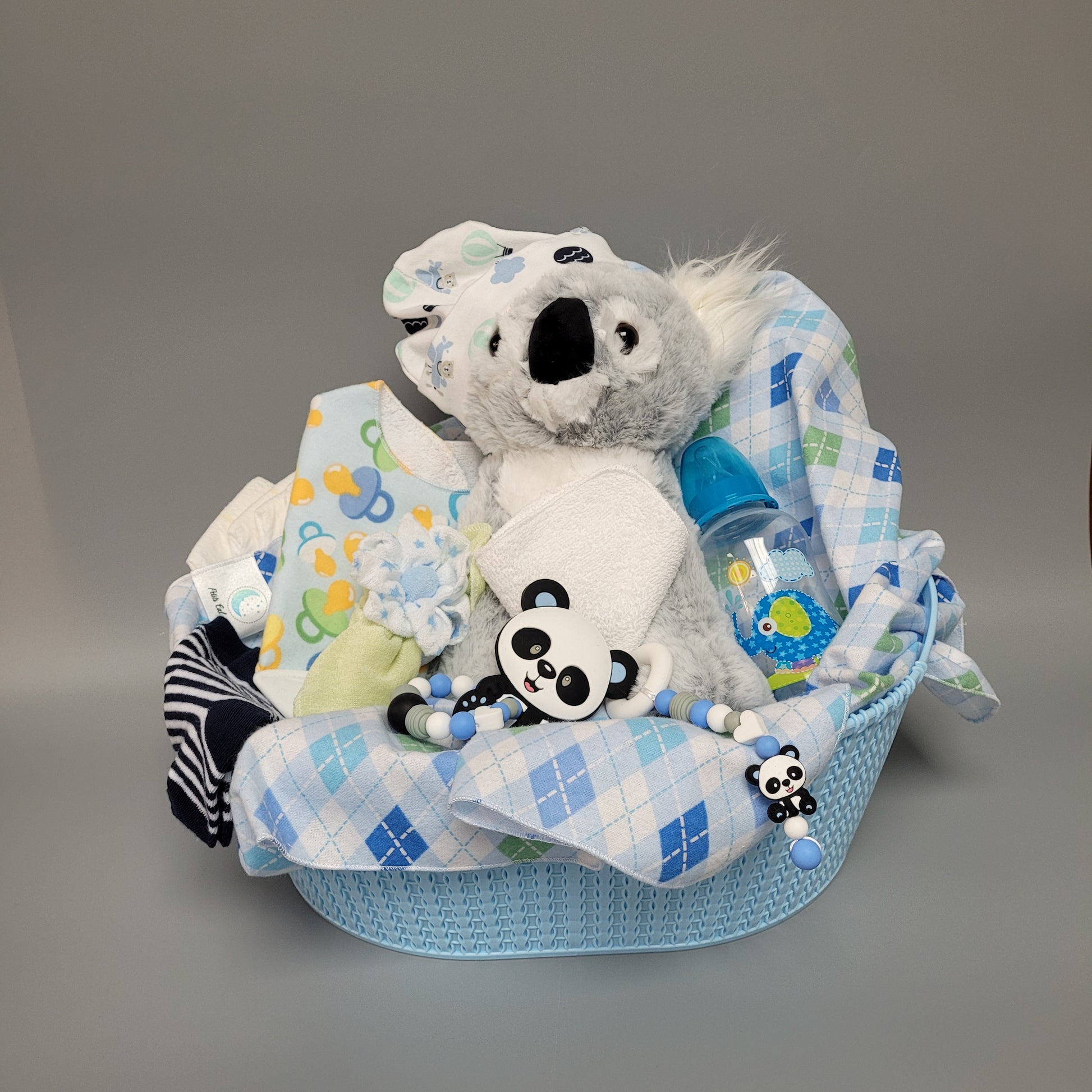 Ensemble cadeau pour babyshower dans un panier bleu avec un toutou koala. Contient une couverture de flanelle bleu un bavoir de dentition, un biberon, des débarbouillettes disposé en fleur, un bonnet, des bas de coton. Contient aussi des couches de bébé de taille #2 et des jouet de dentition en silicone.