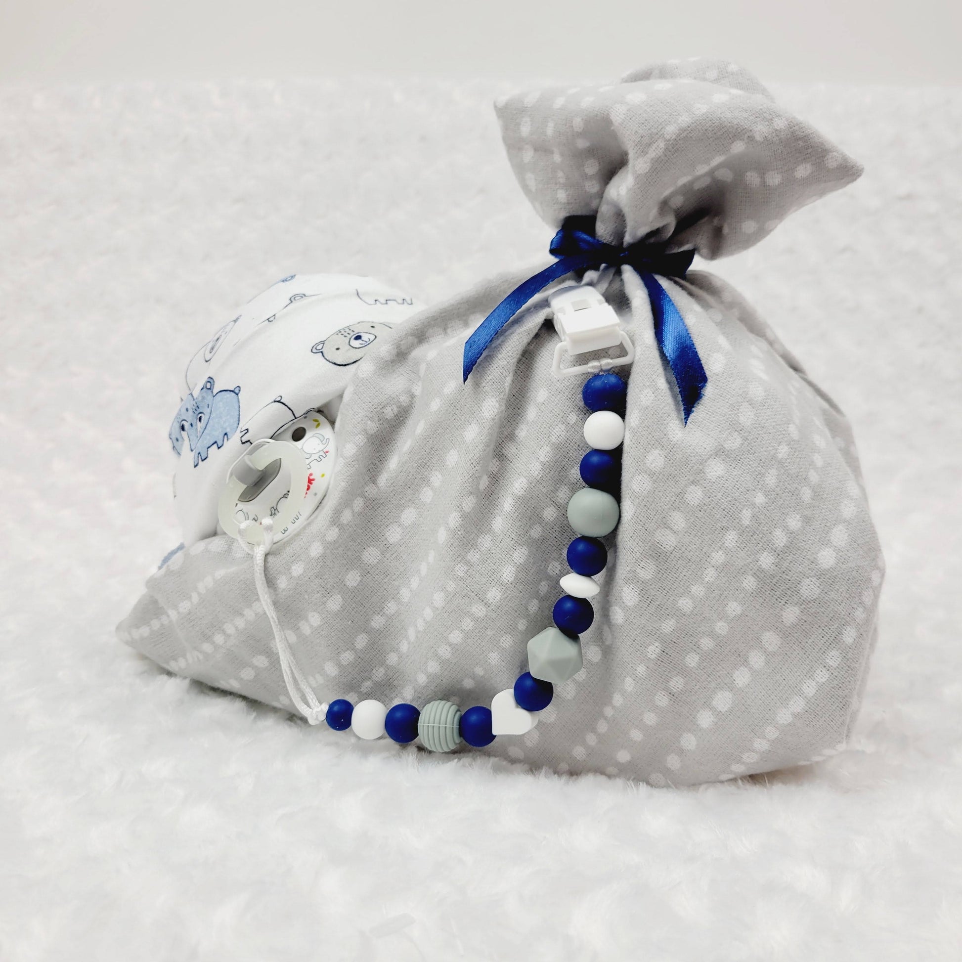 Ensemble cadeau en forme de bébé enveloppé d'une couverture de flanelle grise imprimé de pois blanc. L'ensemble contient des couches pour bébé de taille #2, un bonnet avec des oursons. Un attache-suce en silicone et une suce. 