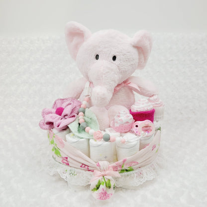 Ensemble cadeau pour babyshower fait de couche pour bébé comme base ou on retrouve un toutou éléphant rose assis entouré de débarbouillettes disposées en fleur et en cupecake. Complété avec une attache-suce et une suce rose.