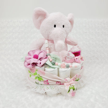 Ensemble cadeau pour babyshower fait de couche pour bébé comme base ou on retrouve un toutou éléphant rose assis entouré de débarbouillettes disposées en fleur et en cupecake. Complété avec une attache-suce et une suce rose.