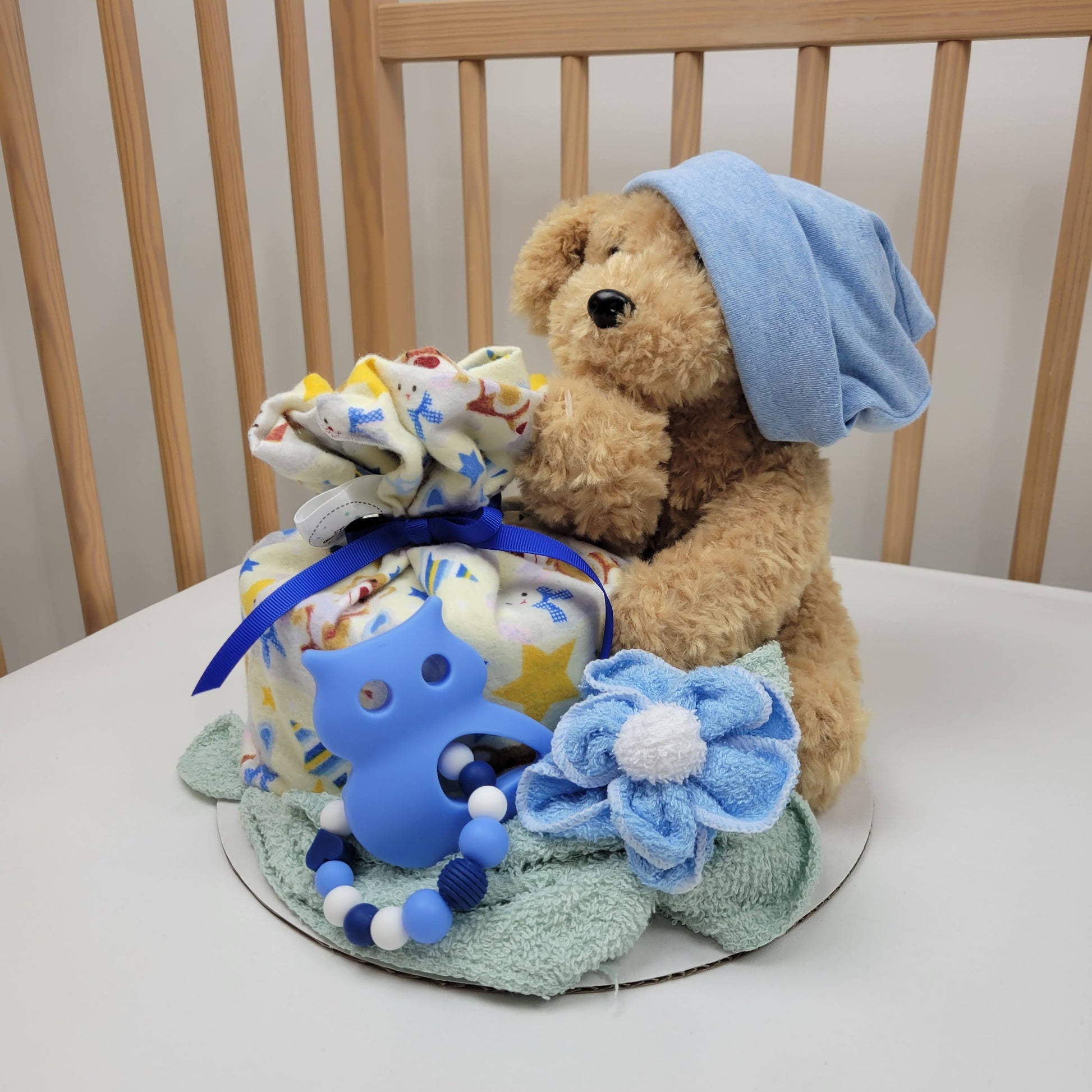 Ensemble cadeau pour babyshower pour bébé garçon. Contenant un  toutou chien beige, une couverture en flanelle jaune, un bonnet bleu, des débarbouillettes et un jouet de dentition avec un hibou bleu.