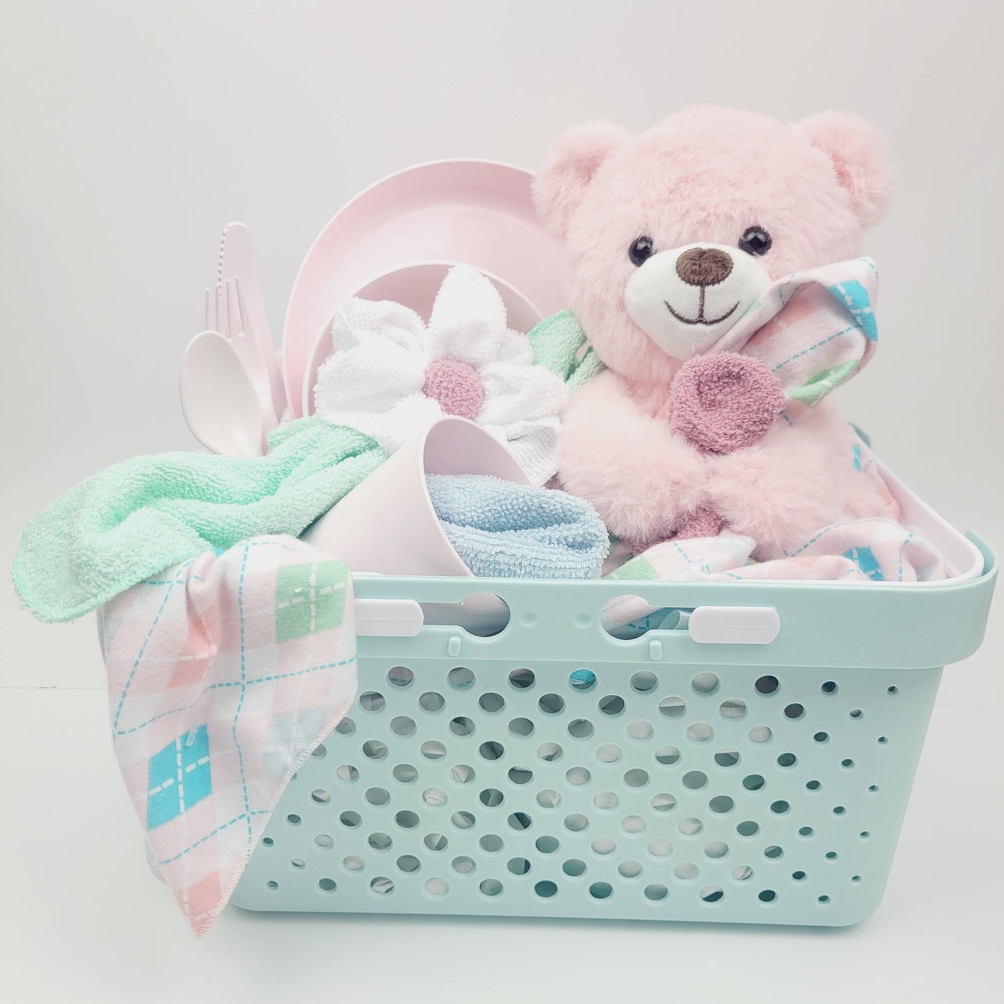 Ensemble cadeau pour babyshower pour bébé fille. Un panier turquoise rempli d'une couverture rose en flanelle avec des débarbouillettes, un toutou ourson rose et en ensemble d'assiette, bol, verre et ustensile rose. 