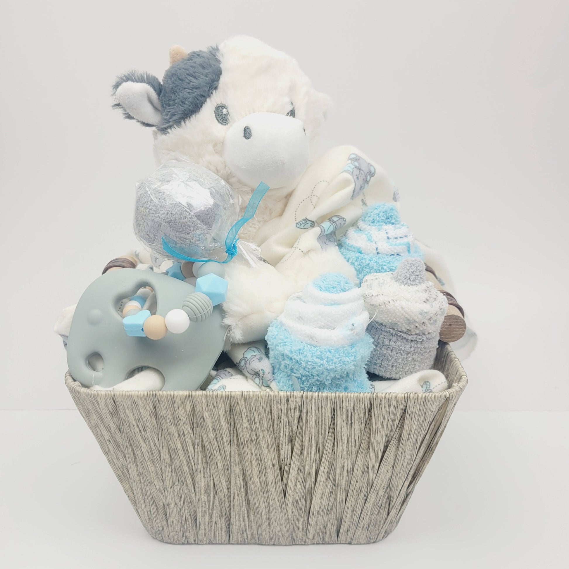 Ensemble cadeau pour babyshower, panier remplis de couverture avec éléphant gris et bleu, un toutou de vache, des cupecakes en débarbouillettes et un jouet de dentition en silicone avec un éléphant gris.