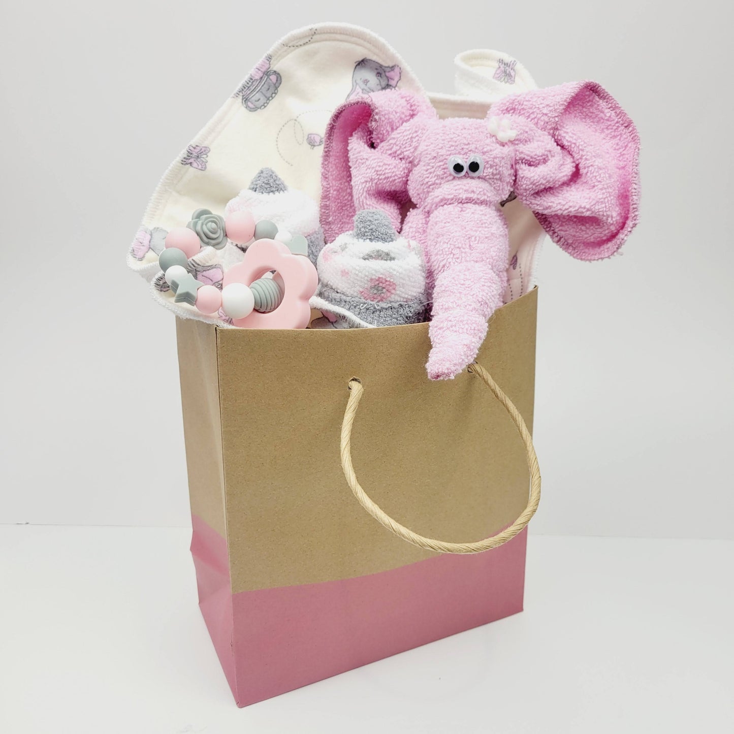 Ensemble cadeau pour babyshower dans un sac cadeau avec la bas du sac rose. On y retrouve un piqué, un jouet de dentition avec une fleur. Un éléphant et un cupcake fait de débarbouillettes.